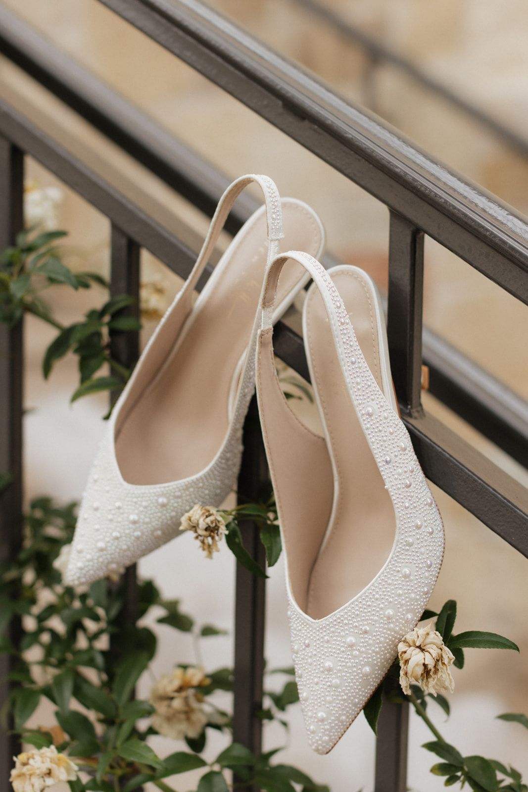 White lace bridal heels with pearl embellishments displayed against a staircase railing with delicate floral accents.