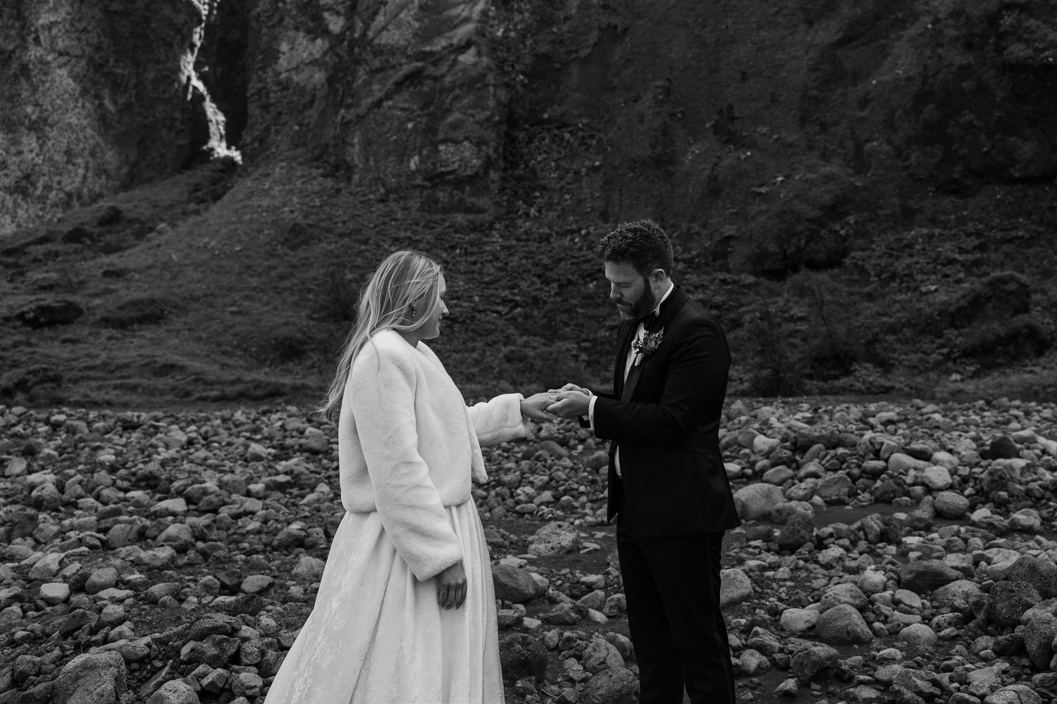black and white photo of groom placing wedding ring on bride's finger after vows in iceland