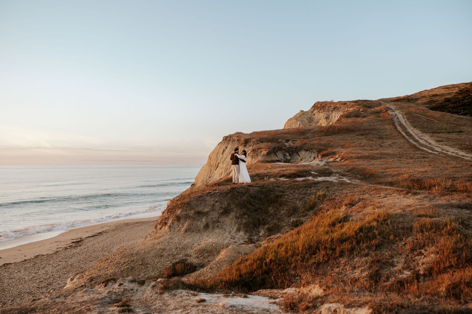couple dancing on a cliff top in half moon bay with the ocean behind them during their sunset engagement photos