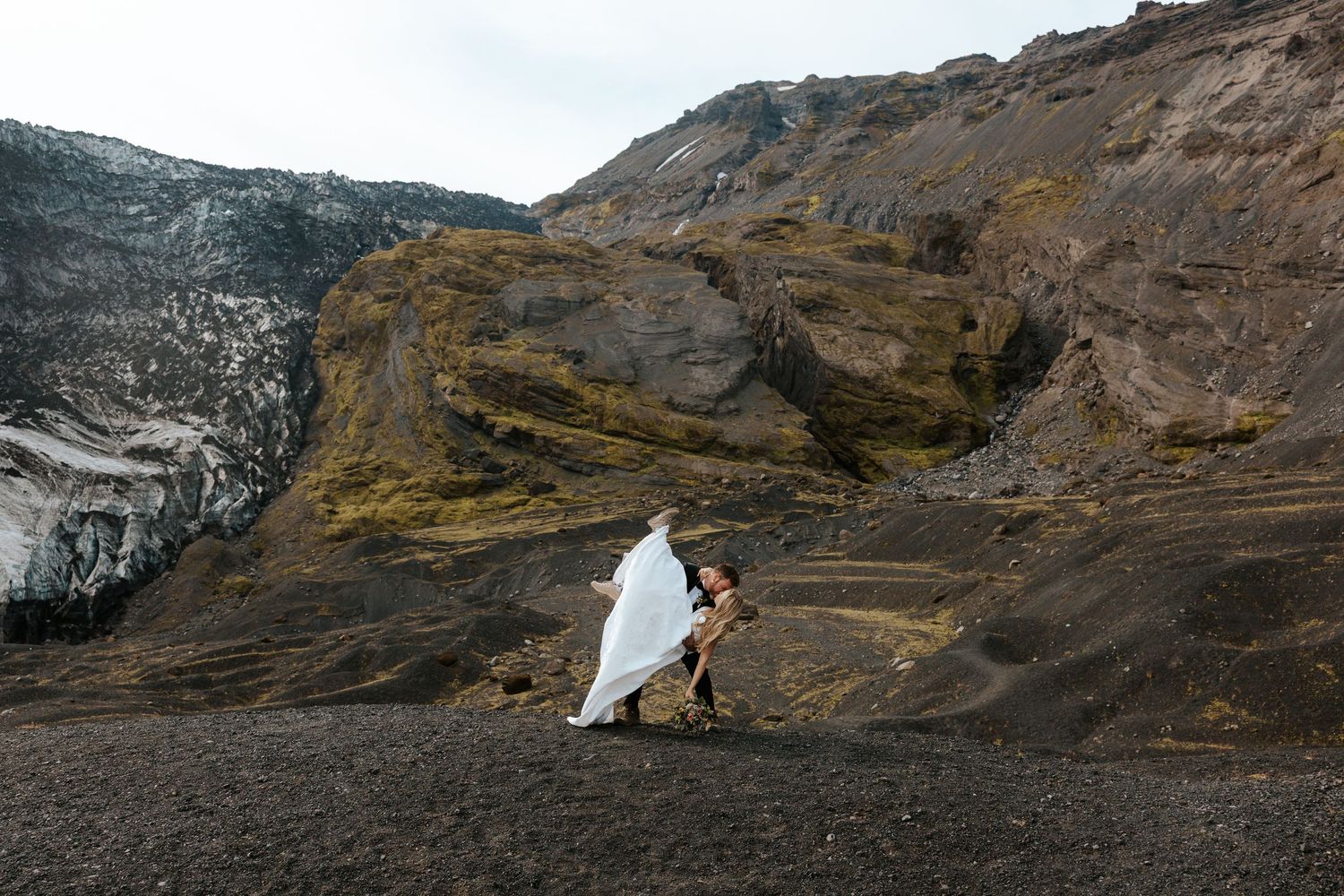 groom dipping bride and kissing her on hill near glacier in Iceland during adventure elopement