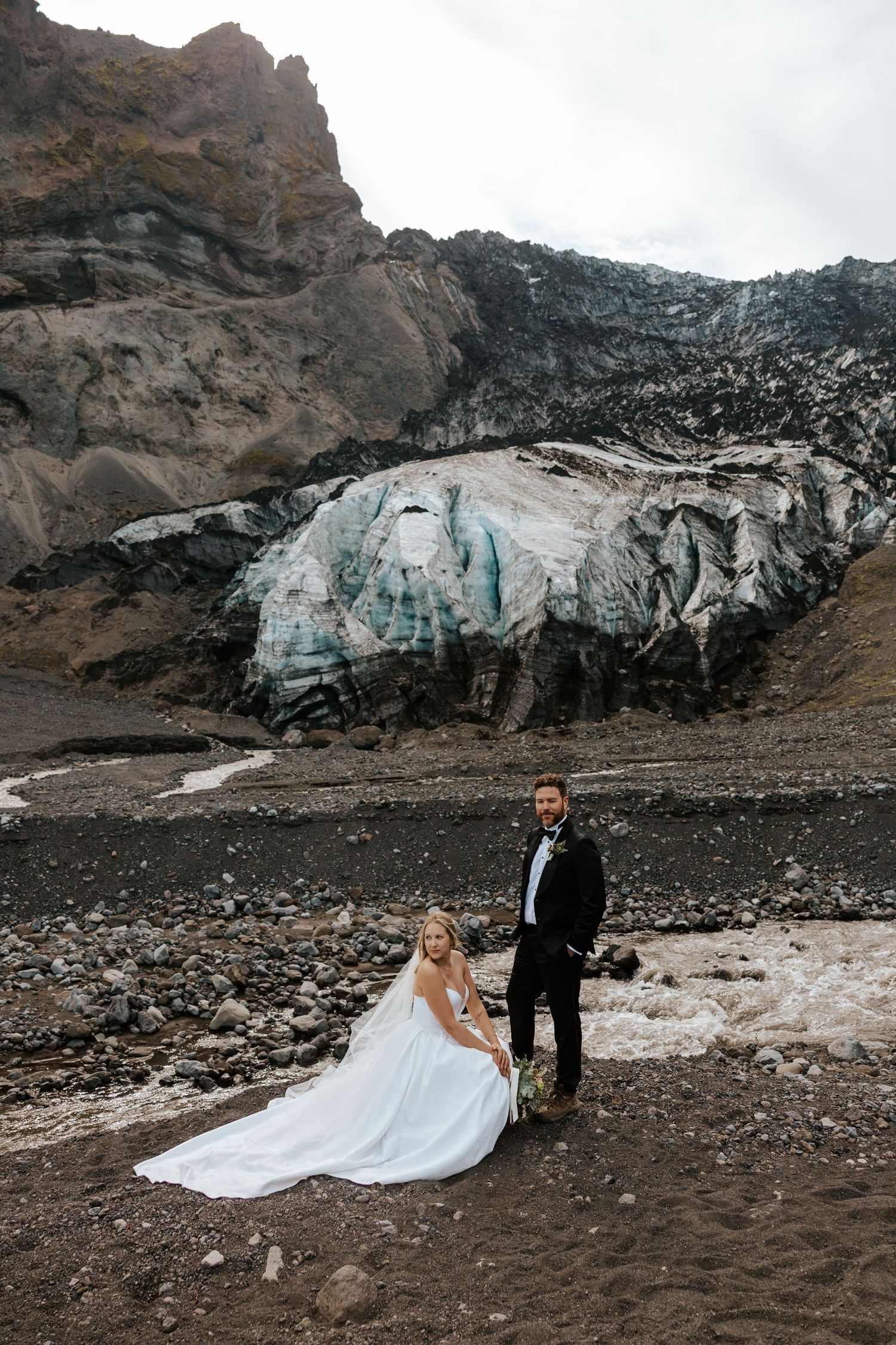 bride crouching down next to groom in front of glacier in Þórsmörk (Thórsmörk), Iceland during Iceland elopement