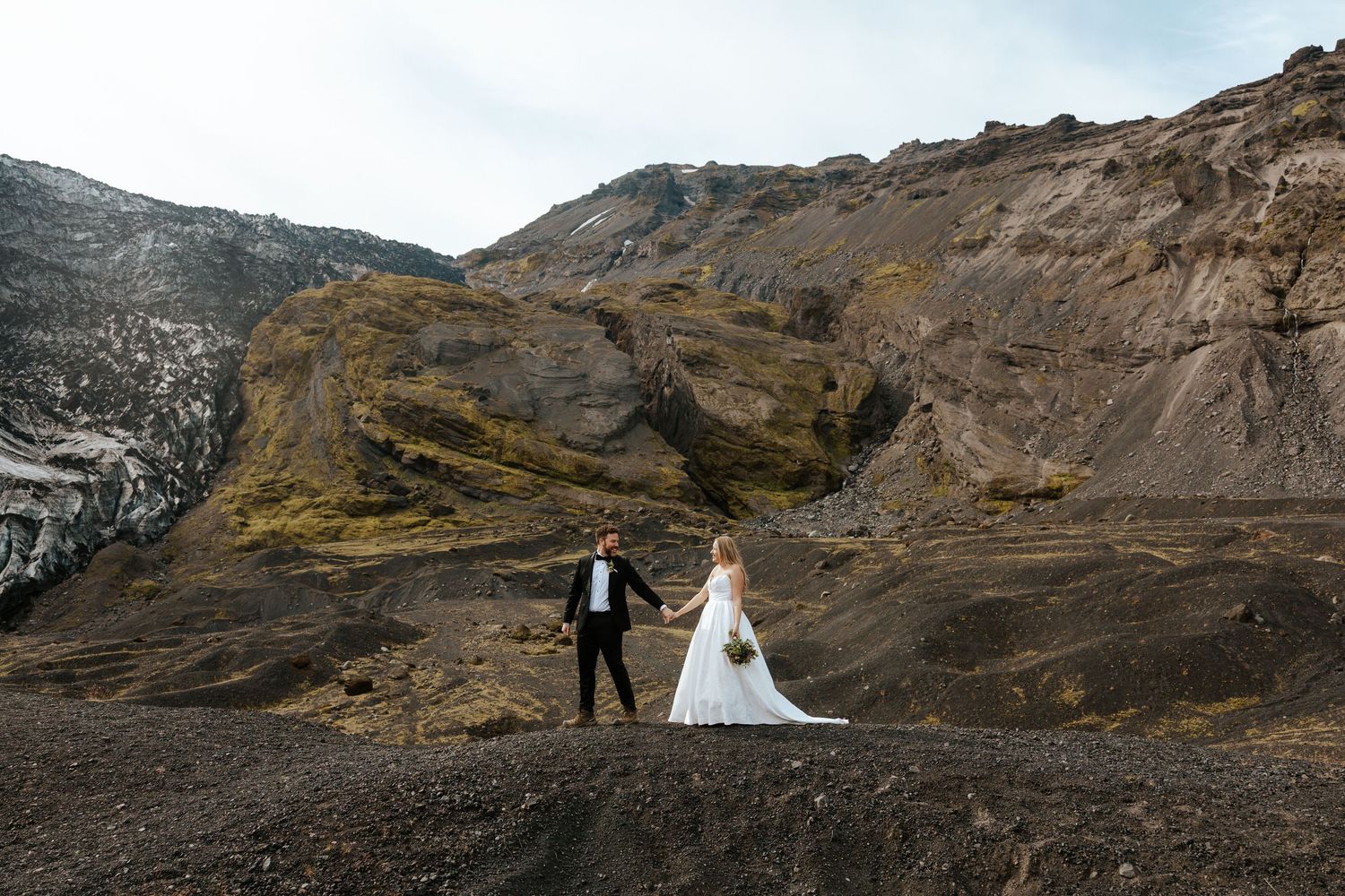 groom and bride walking across a hill towards glacier in a mountain in Þórsmörk (Thórsmörk), Iceland during their Iceland elopement day