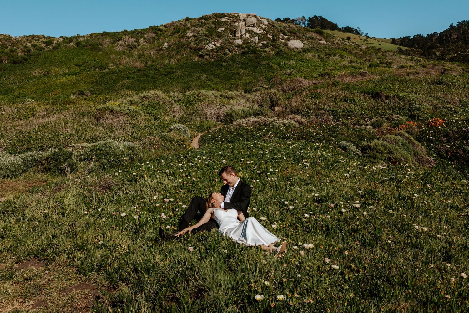 groom and bride sitting in a field of flowers during Carmel elopement day
