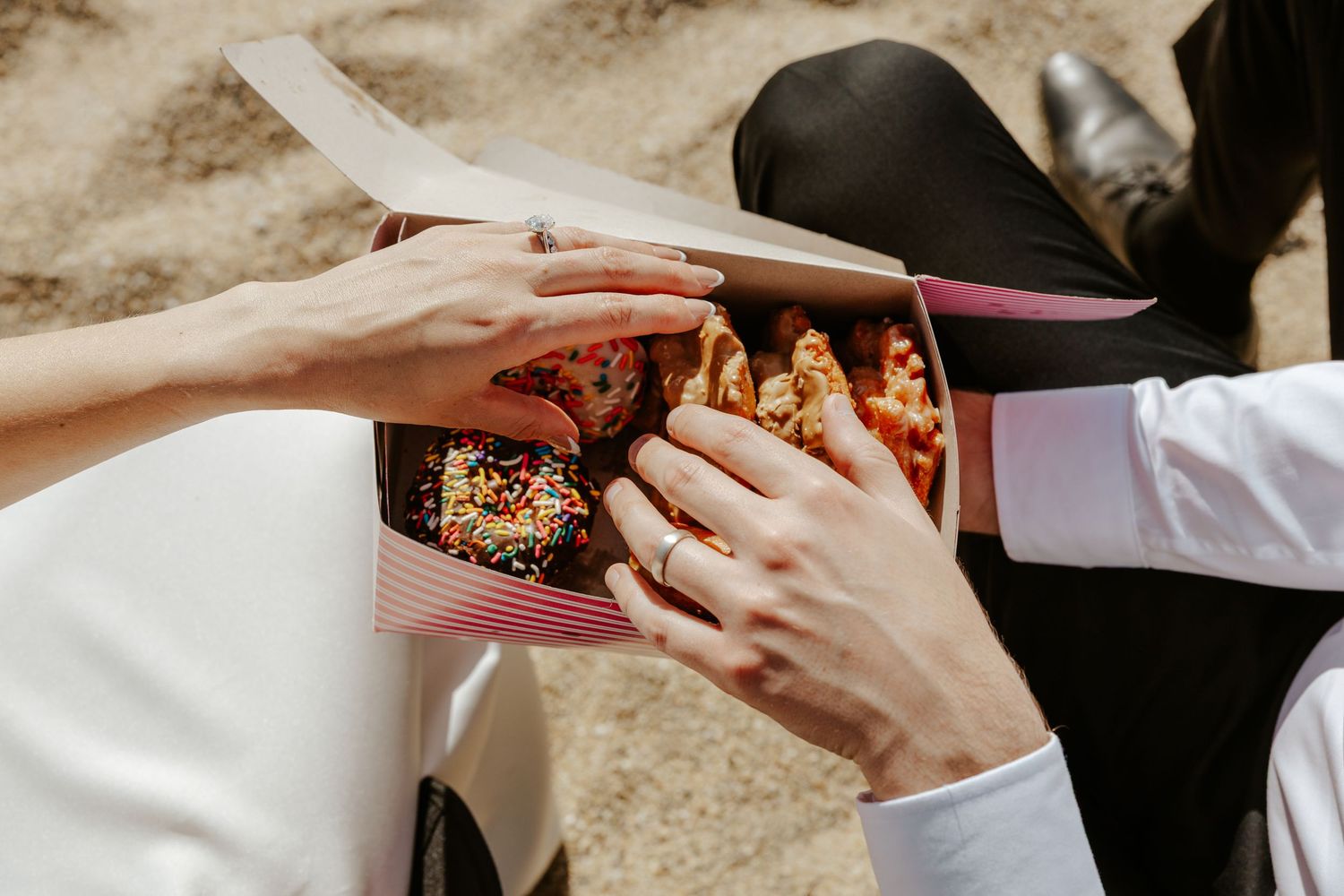 hands reaching into donut box while at the beach