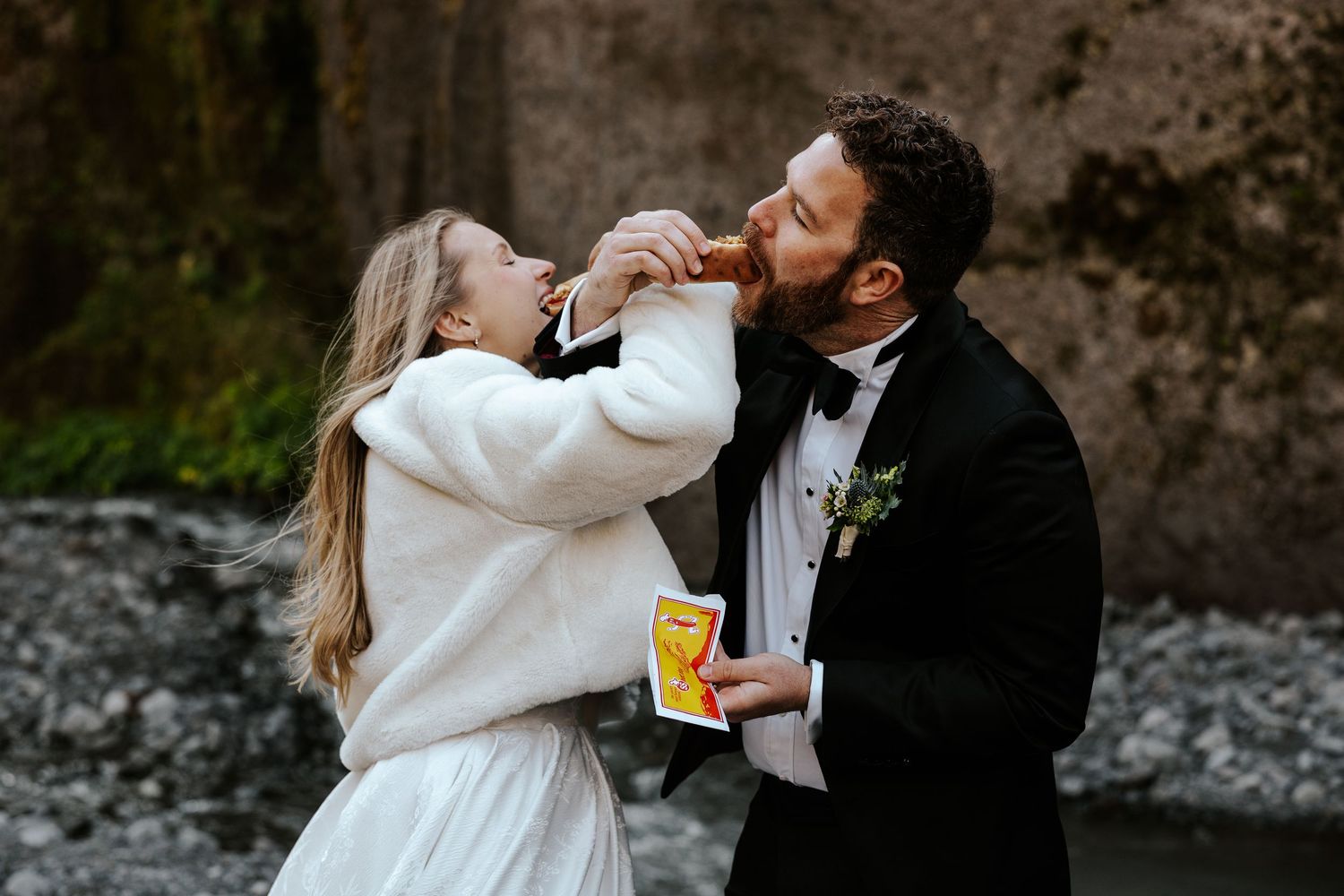 bride and groom interlocking arms and taking a bite of their hot dogs in iceland