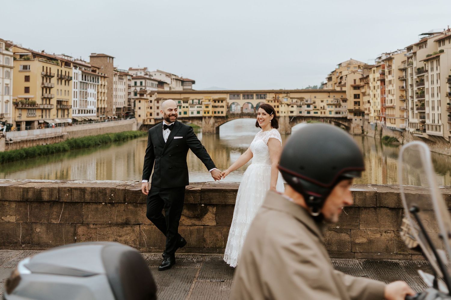 couple walking in florence, italy with view of ponte vecchio during their sunrise italy elopement in tuscany
