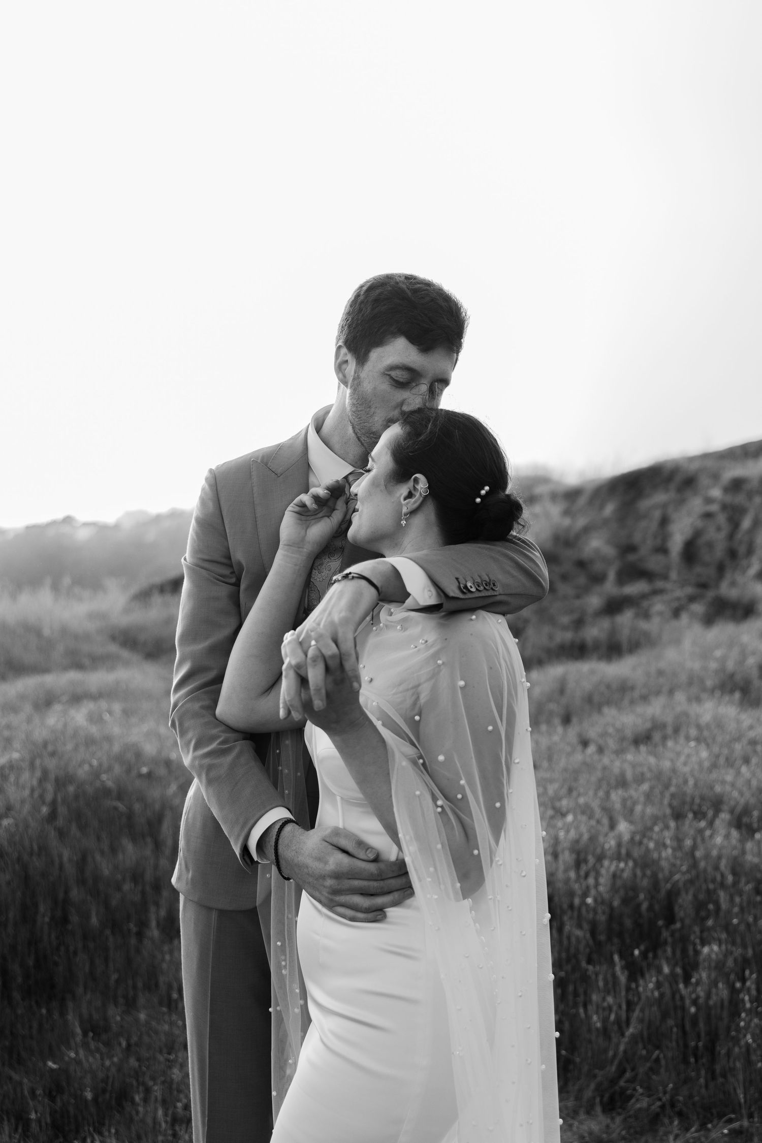 Black and white photo of groom kissing his bride's forehead on a cliffside while near San Francisco, California