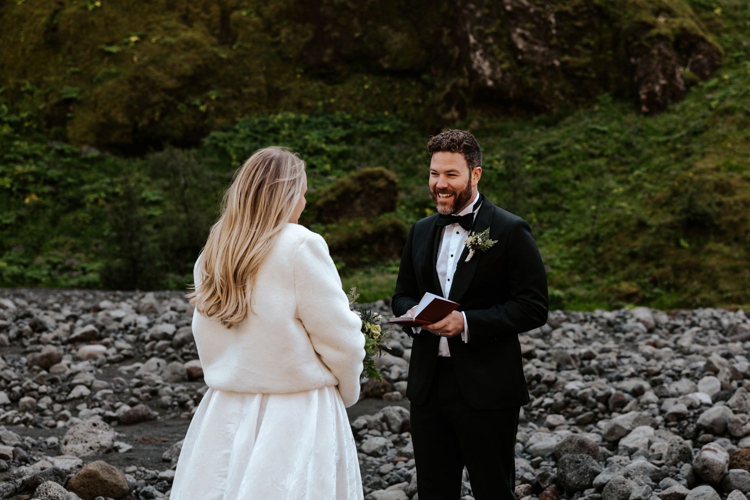 candid of groom smiling and laughing at bride while he shares his vows with her in iceland