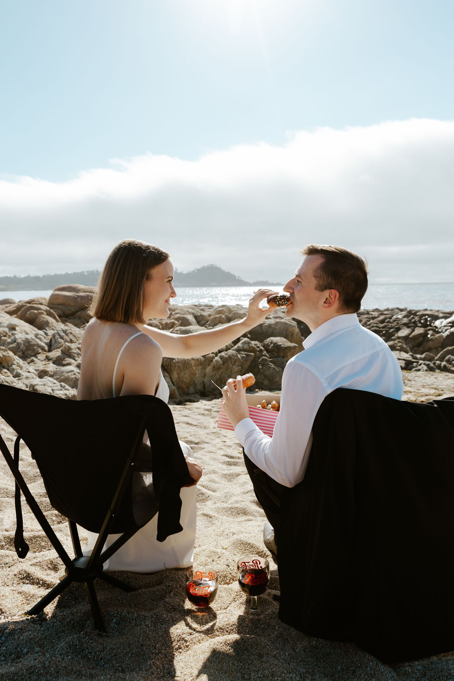 bride feeding donut to groom while sitting in camping chairs during beach elopement in Carmel, California