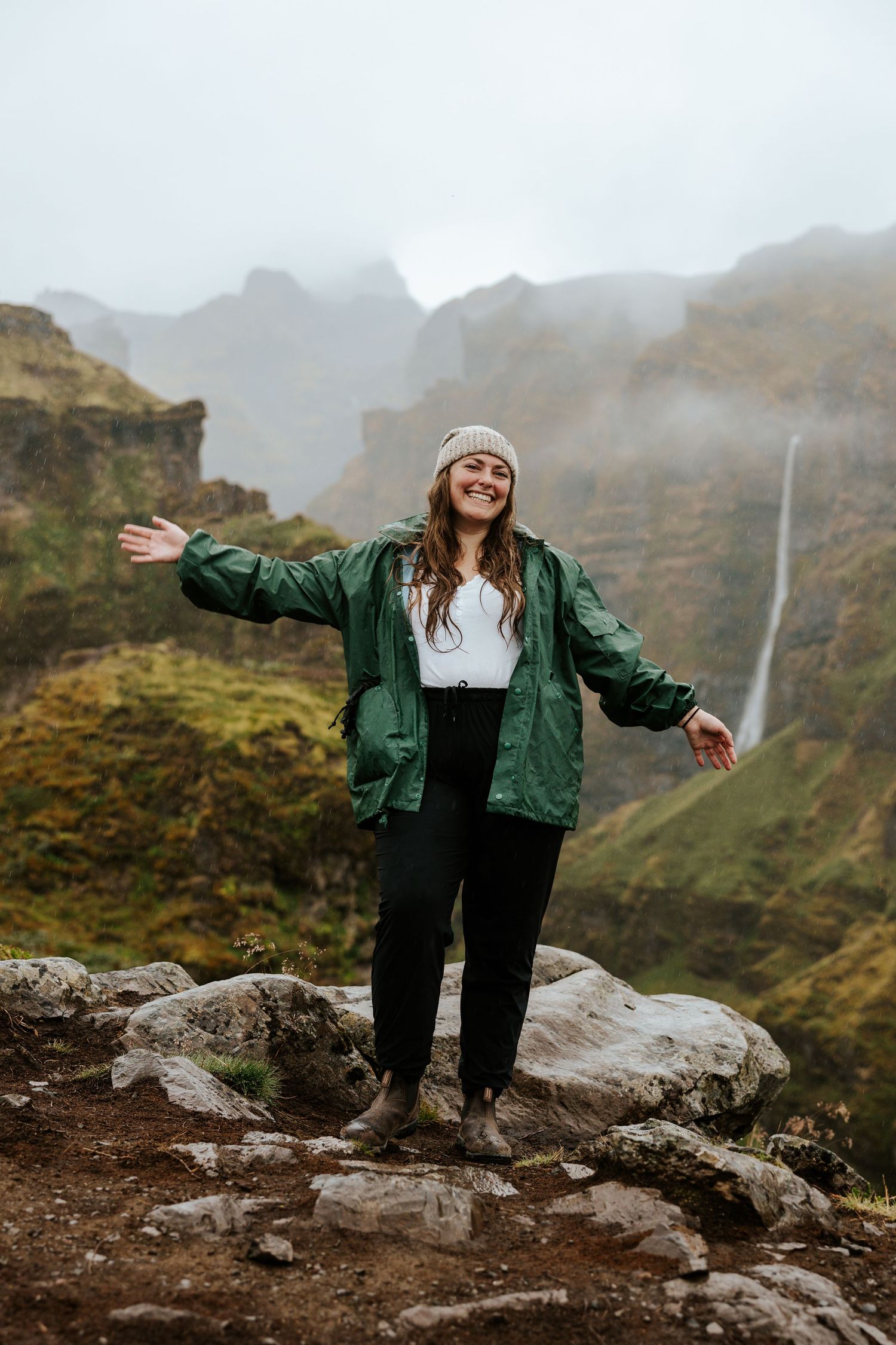 iceland photographer standing on a mountain with a view of a canyon and waterfall while it rains