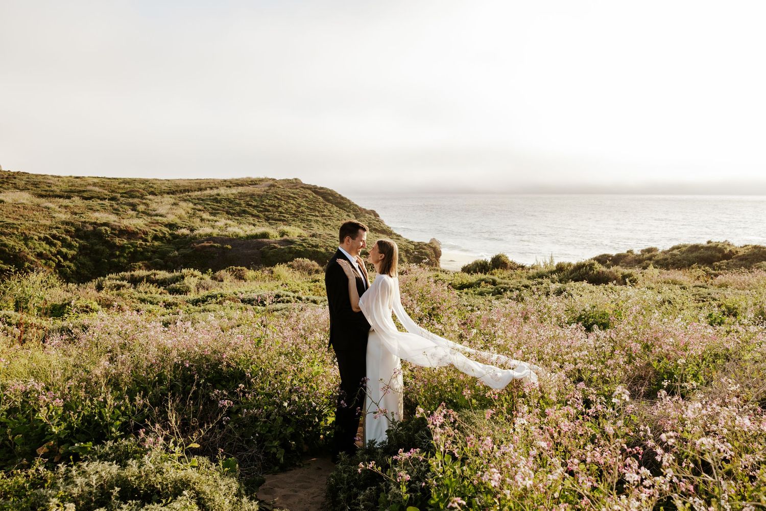 couple looking at each other and standing close in a field of flowers on a clifftop in northern california