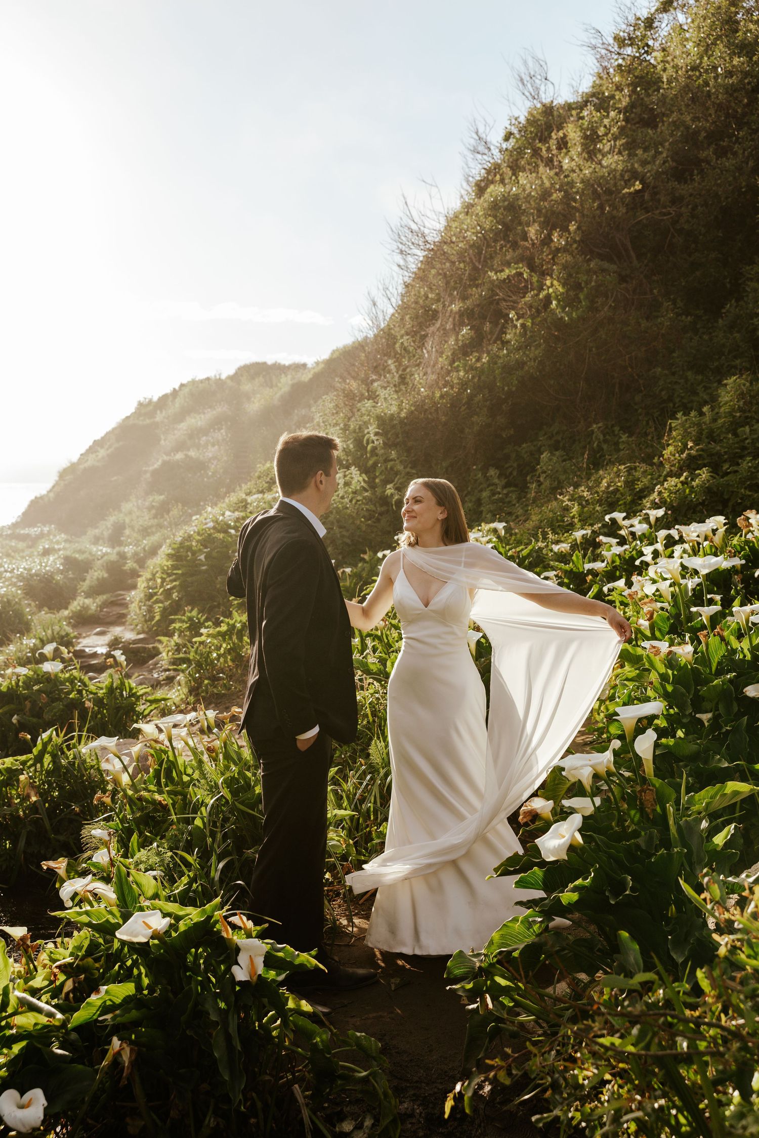 bride twirling her dress while holding groom's hand in calla lily vallery during coastal elopement