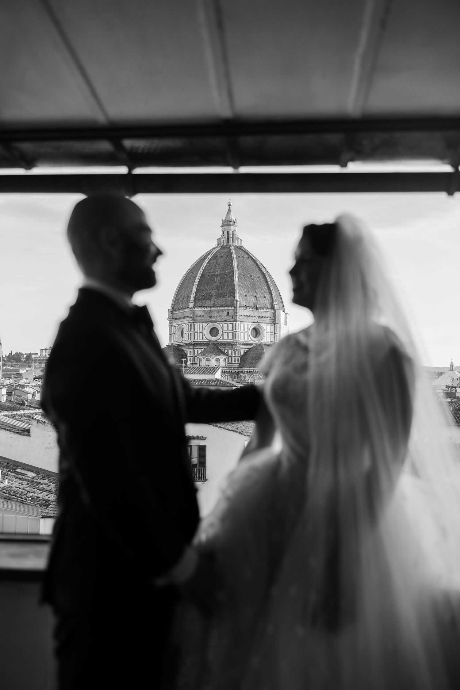 black and white photo of couple looking out the window towards the Duomo in Florence at sunset on their all day italy elopement in tuscany