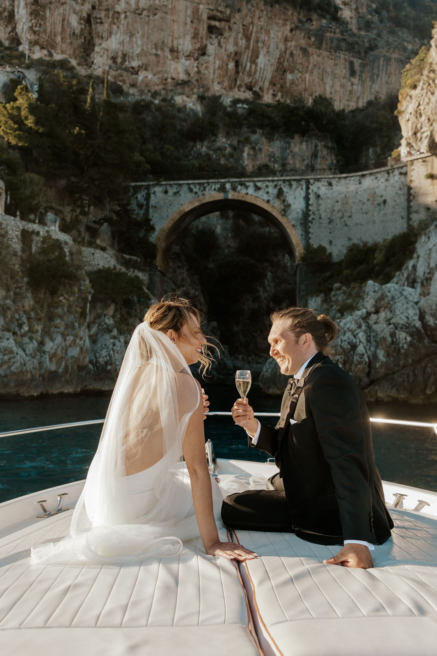 eloping couple sitting on the front of a boat drinking champagne along the amalfi coast during their positano elopement day