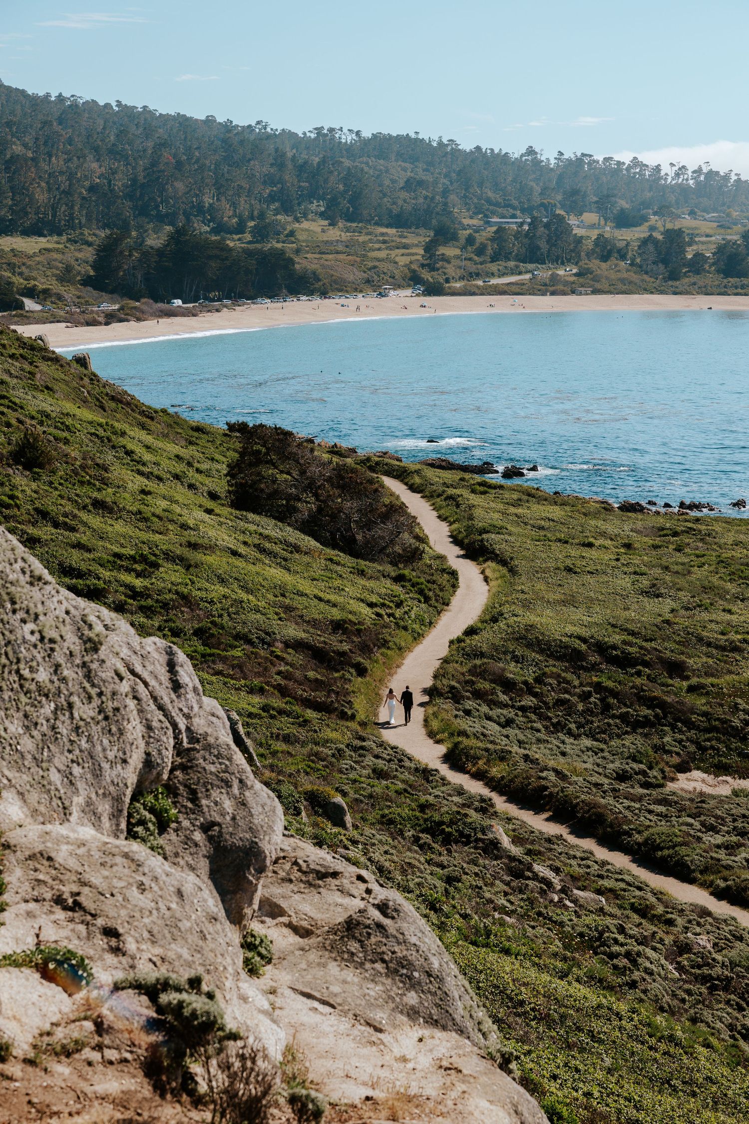 couple walking along a pathway on the coast with ocean behind them