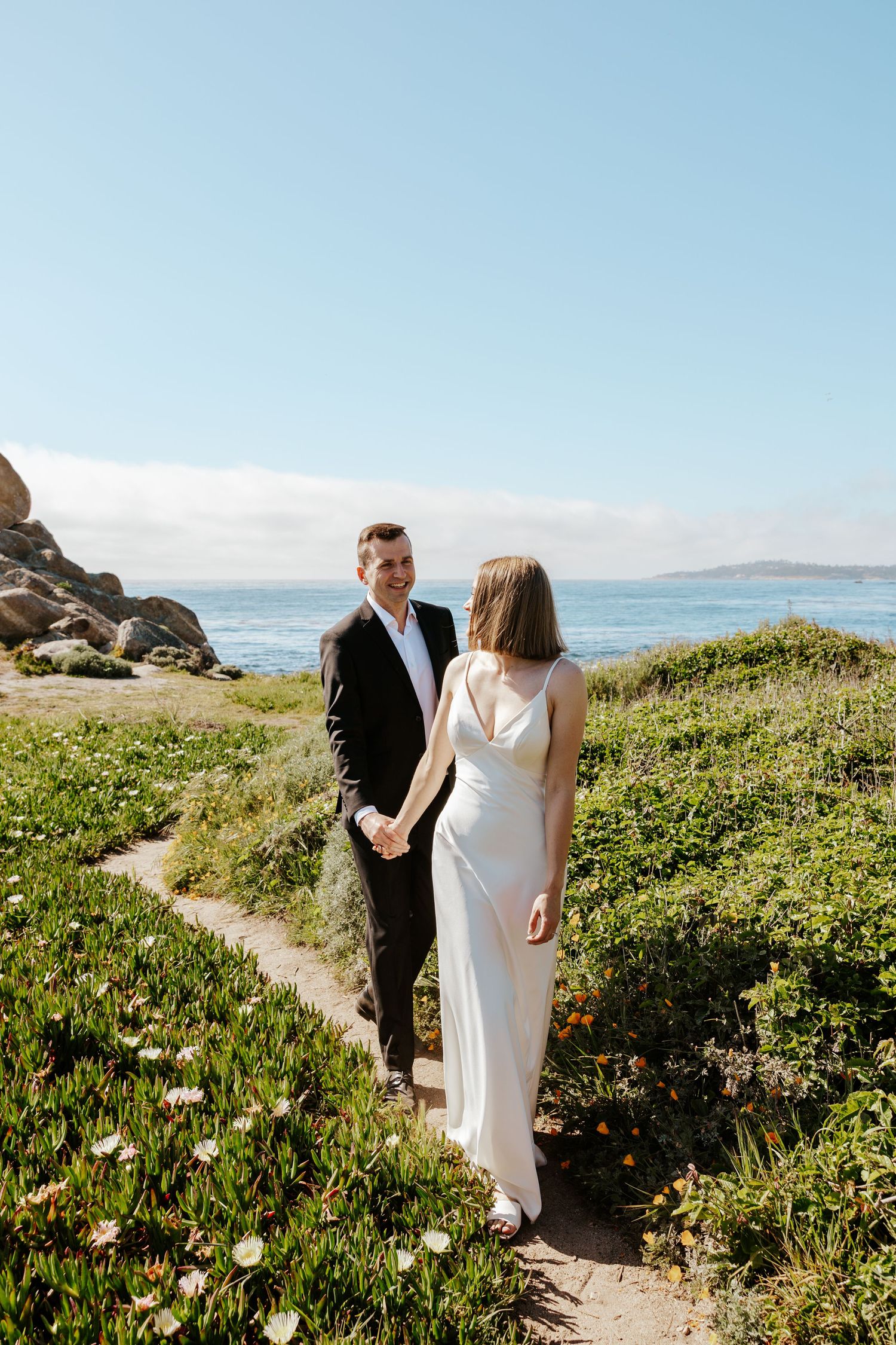 candid of bride and groom walking on a cliff during Carmel coastal elopement