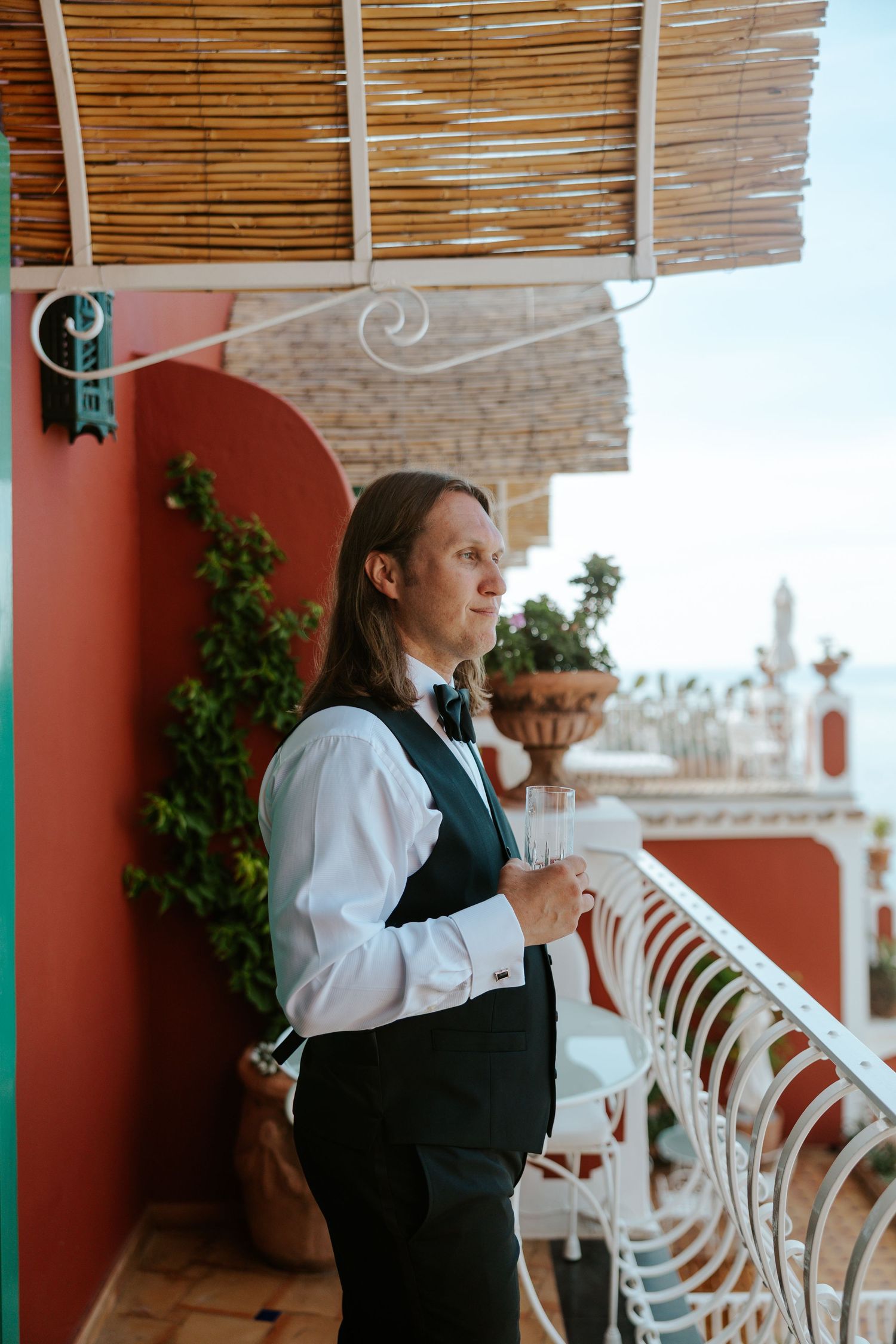 groom looking out over le sirenuse hotel balcony on positano elopement day while drinking beer