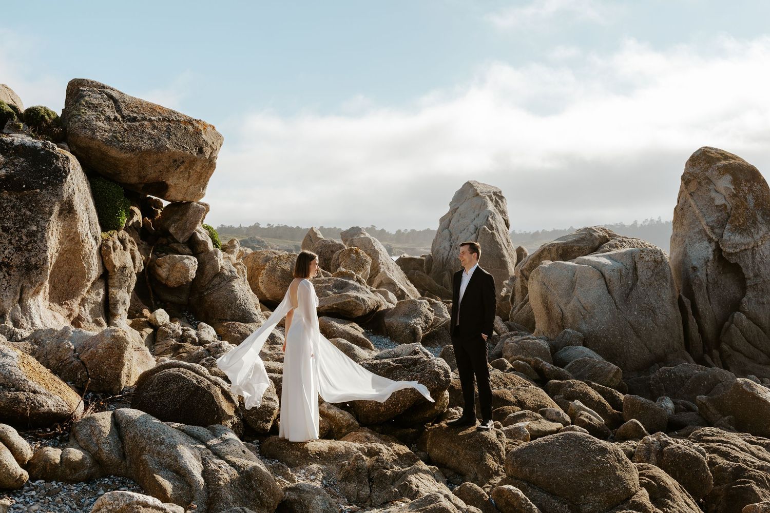 bride and groom climbing over coastal rocks during beach elopement