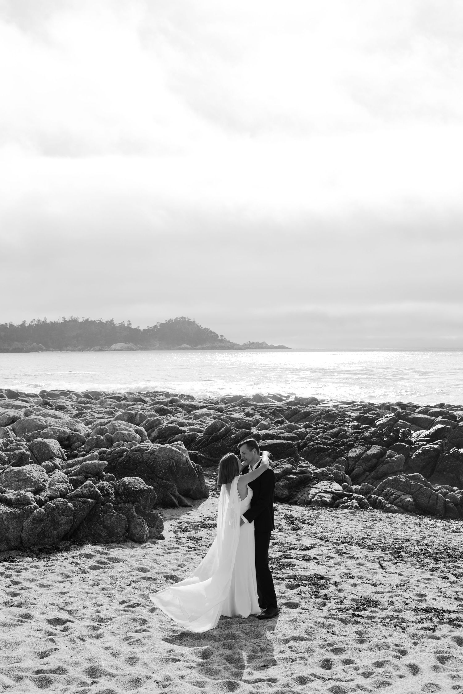 black and white photo of bride and groom embracing on the beach