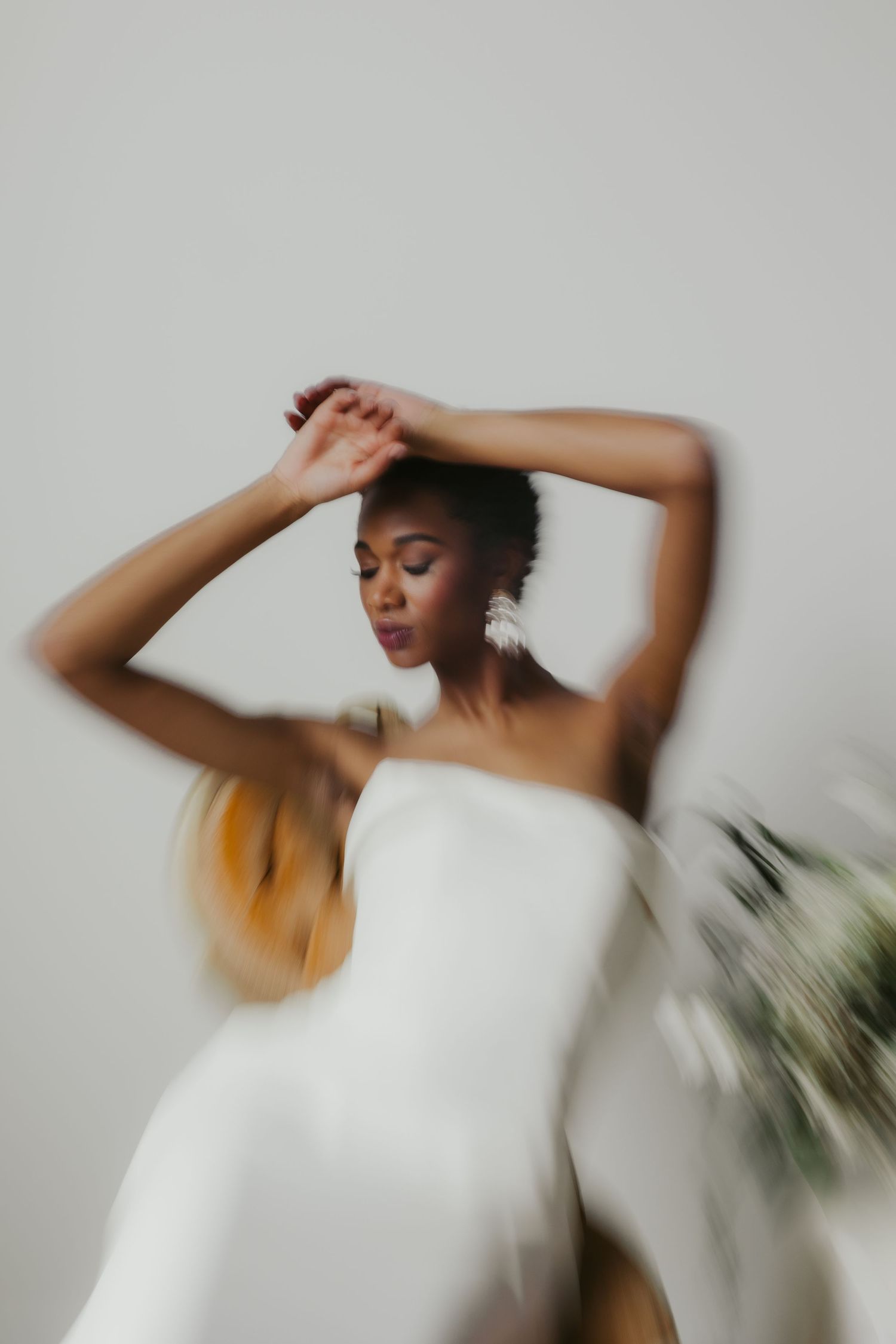 Artistic motion-blurred portrait of person in white dress against neutral background with soft dreamy aesthetic.
