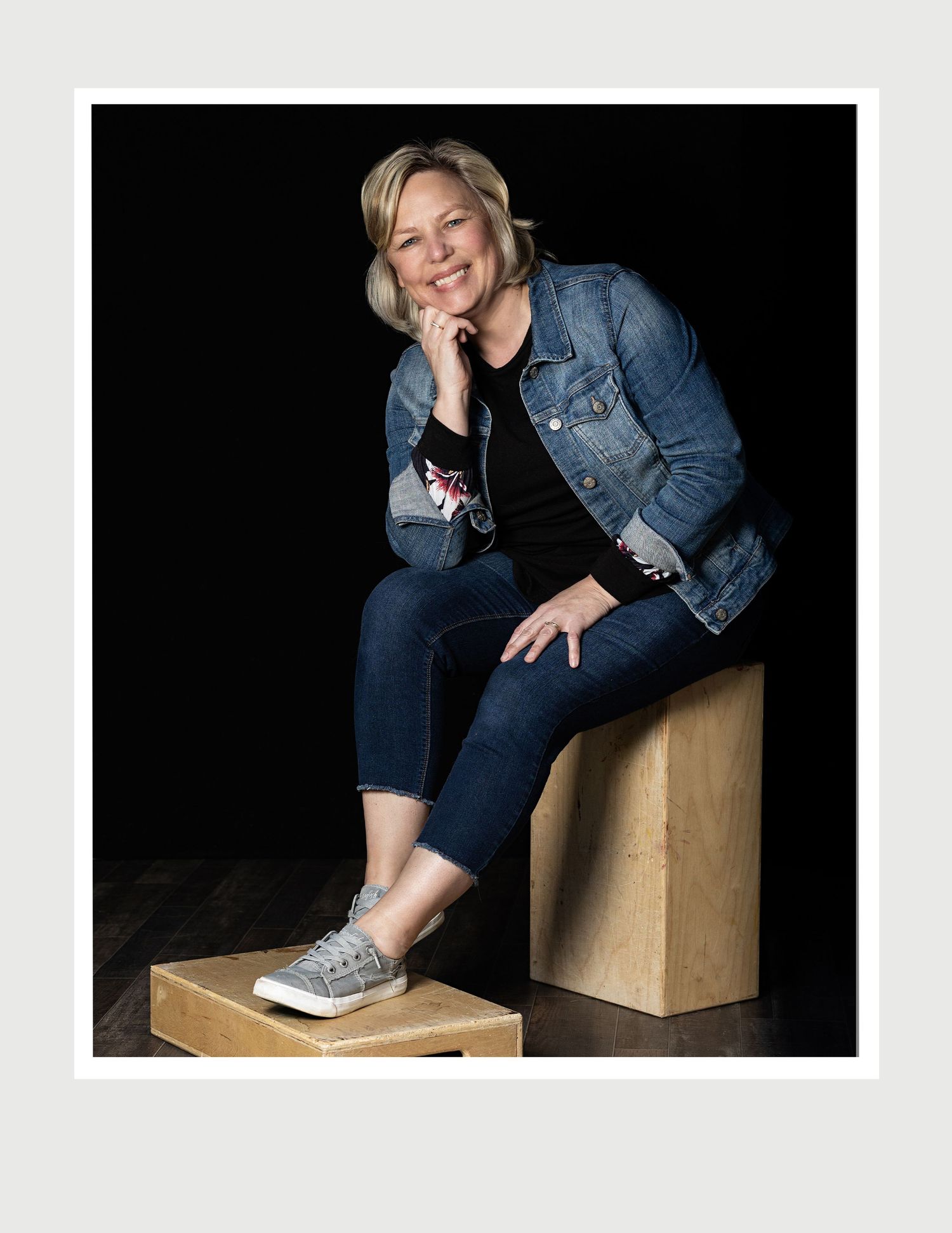 Professional portrait of photographer sitting on wooden blocks against black background.