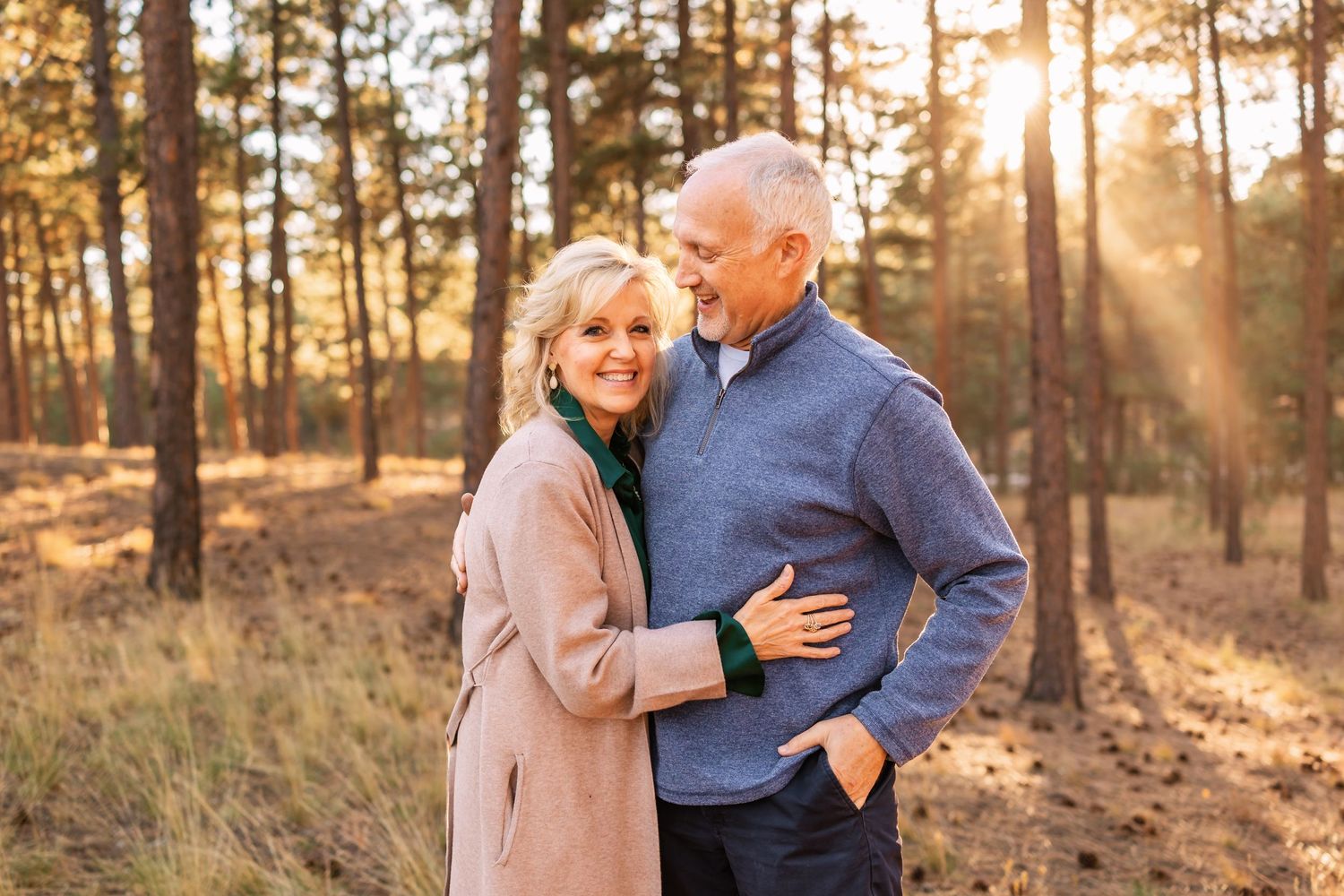 Affectionate couple embraces in sunlit forest during golden hour wearing cozy sweaters and autumn attire.