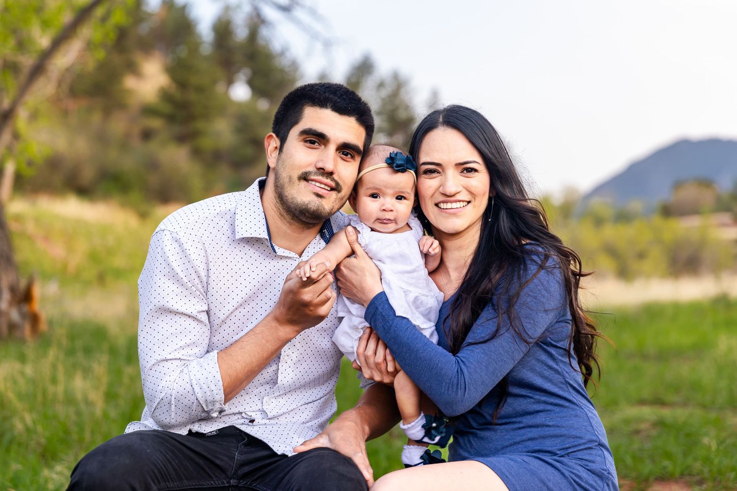 Happy family enjoying time together on grassy hill with mountain scenery in background.