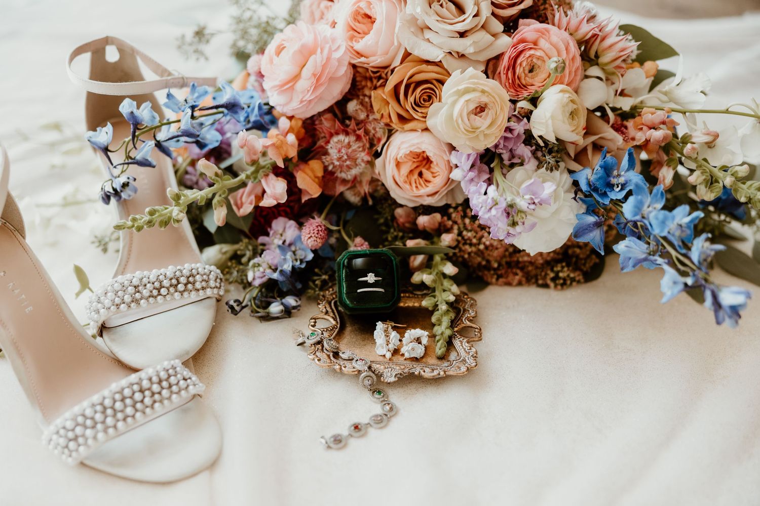 Romantic wedding bouquet with pink roses, blue delphinium, and crystal accessories.