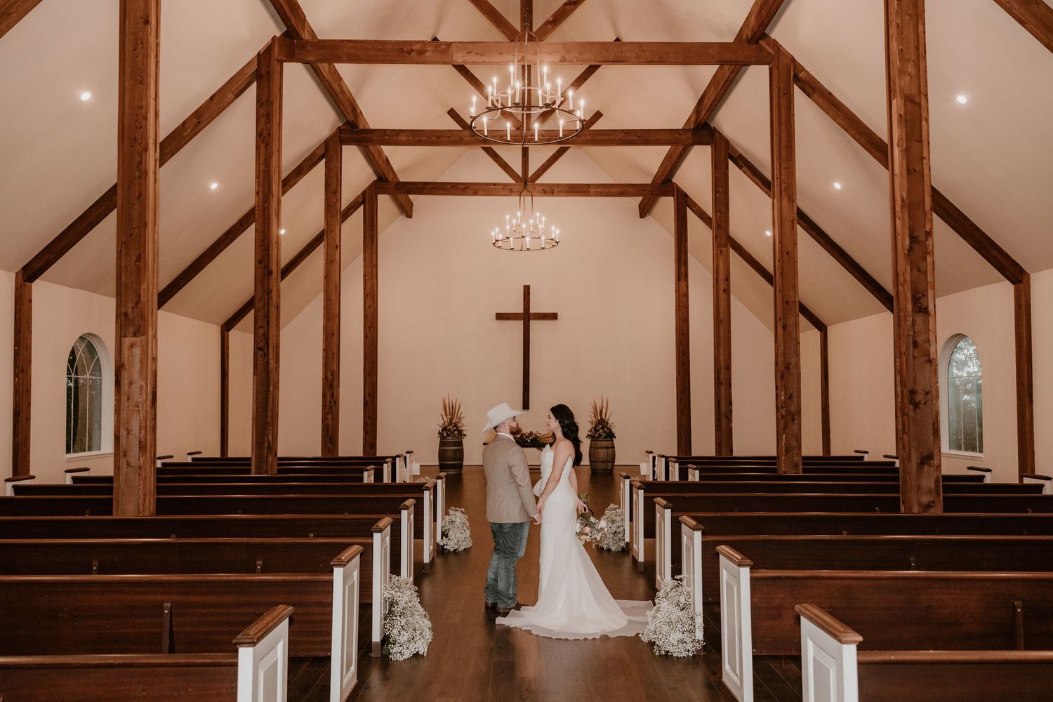 Interior of rustic wooden church with exposed beams and chandeliers during wedding ceremony.