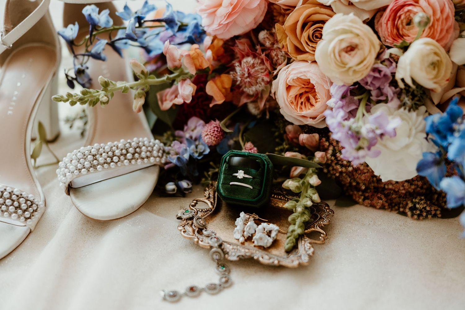 Wedding accessories and jewelry arranged with colorful floral bouquet featuring roses and delicate details.