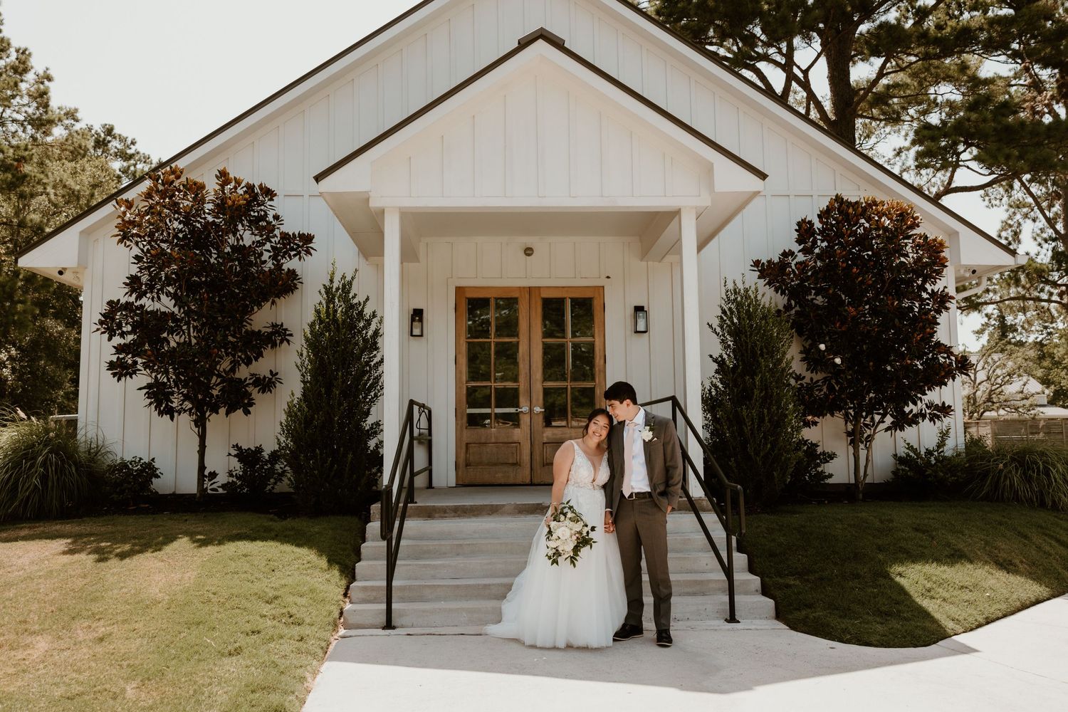 Modern white chapel wedding venue with wooden doors and landscaped entrance.