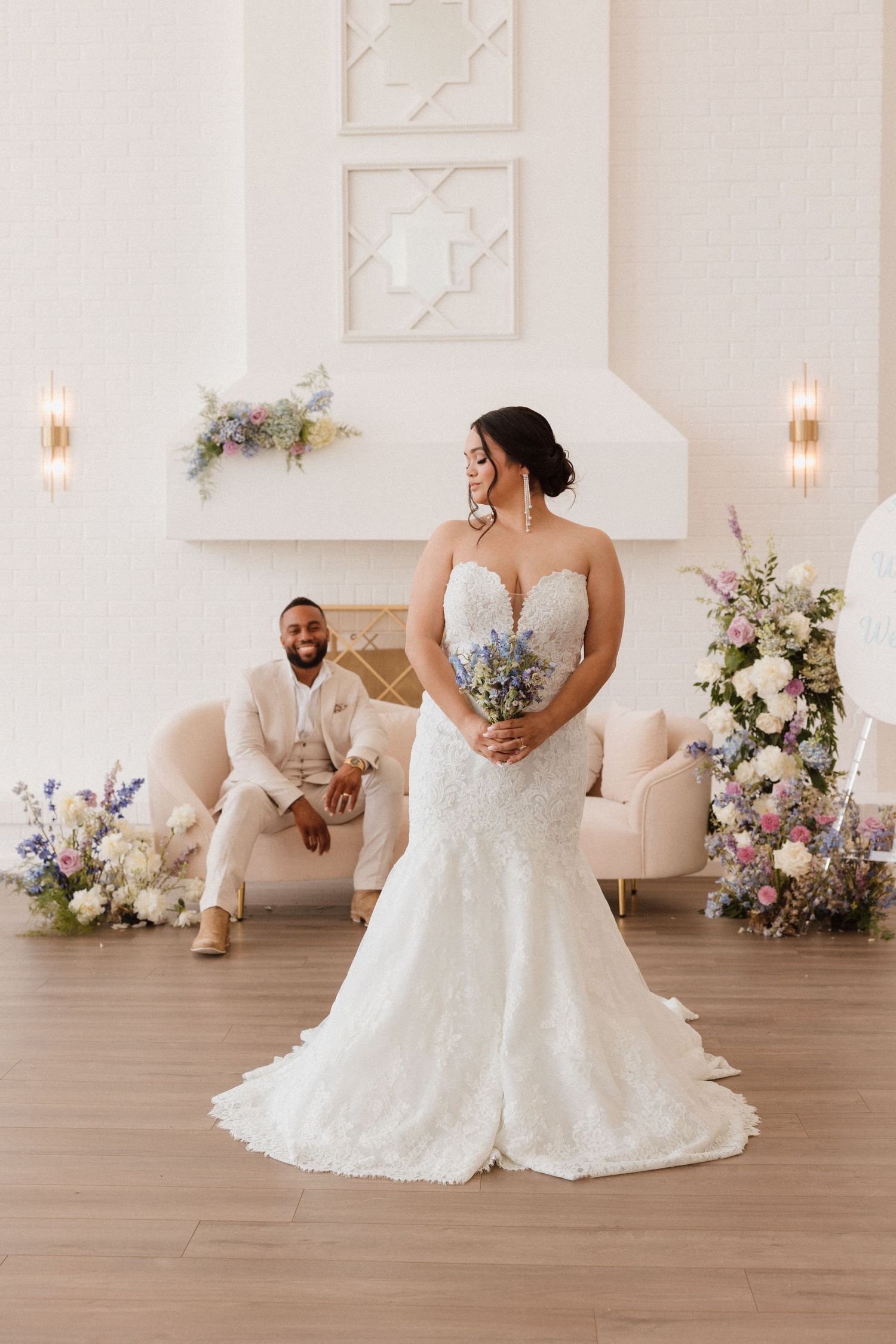 Elegant wedding portrait in white room with floral arrangements and soft lighting.
