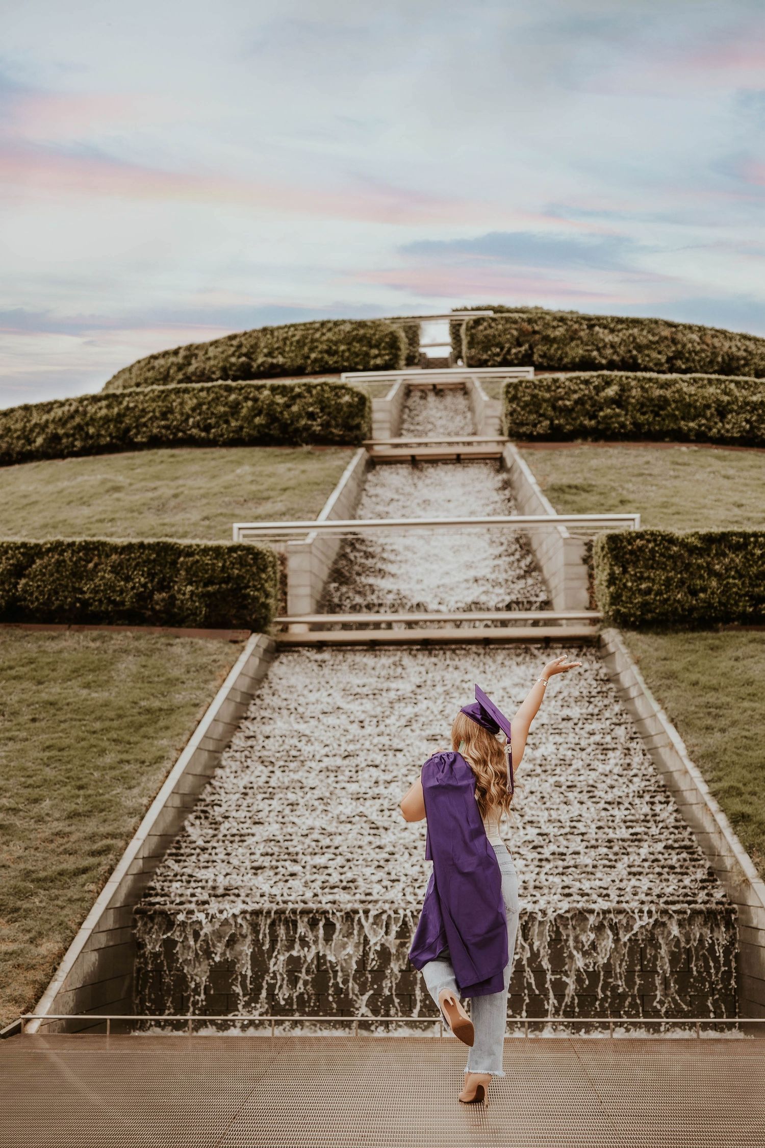 Person in purple dress dancing on geometric water feature at ornate garden terrace during sunset.