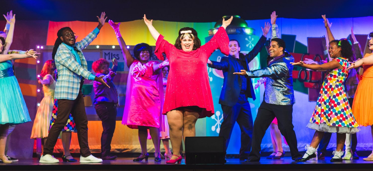 A photo from a production of Hairspray. The cast is together in a pose at the end of a song.