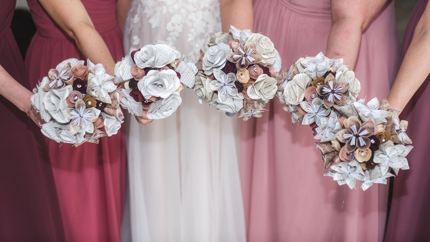 A bride and her bridesmaids holding bouquets. The bouquets are made of folded sheet music.
