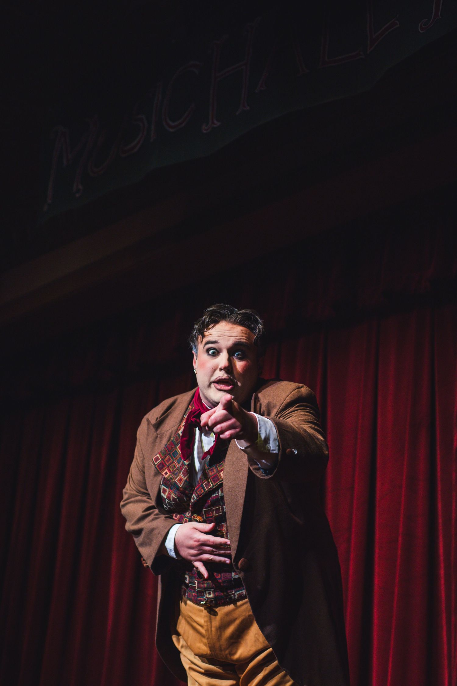 A photo from a production of The Mystery of Edwin Drood. The actor featured is pointing at the camera.