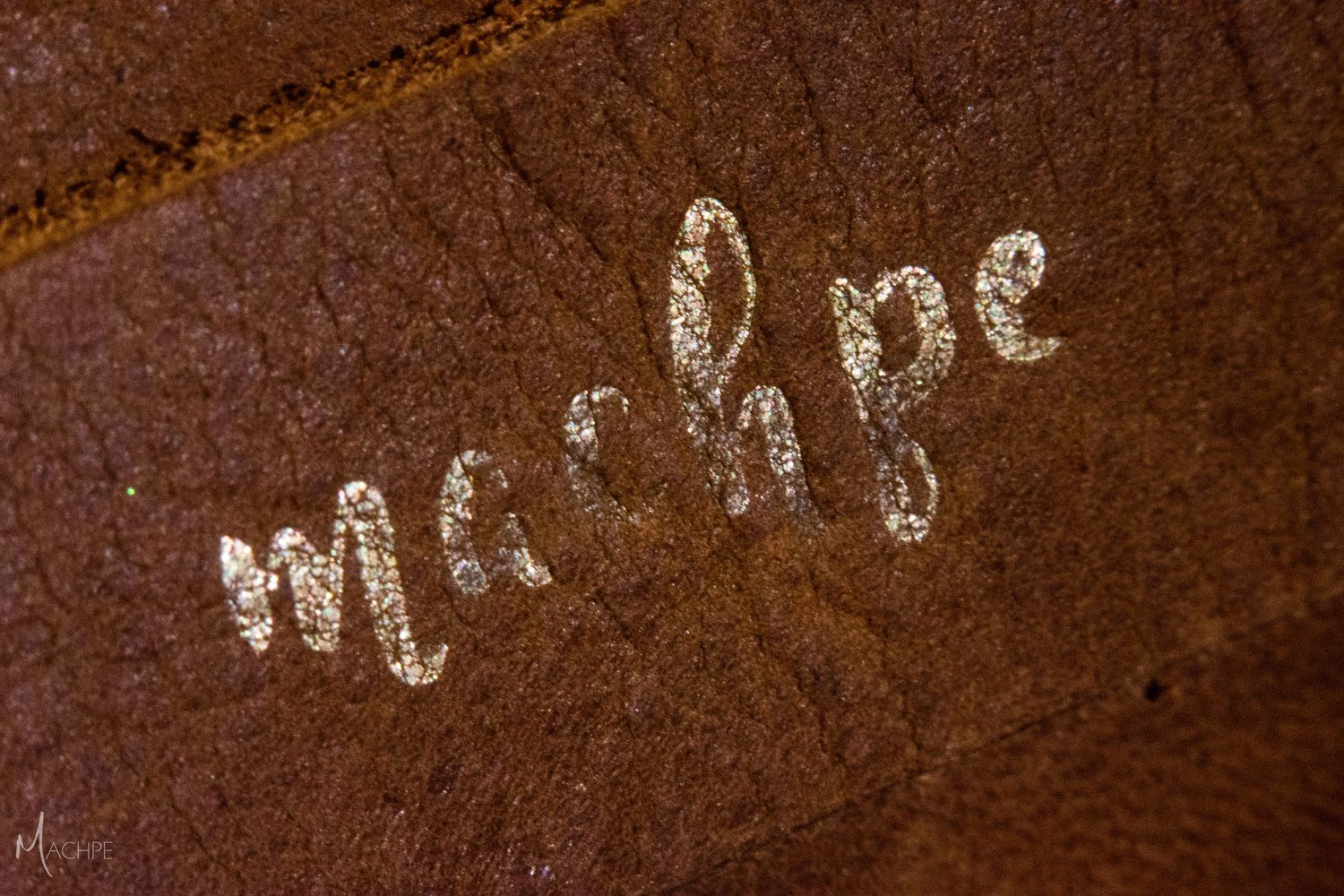 A leather camera strap with machpe printed in gold cursive, the letters faded with age.