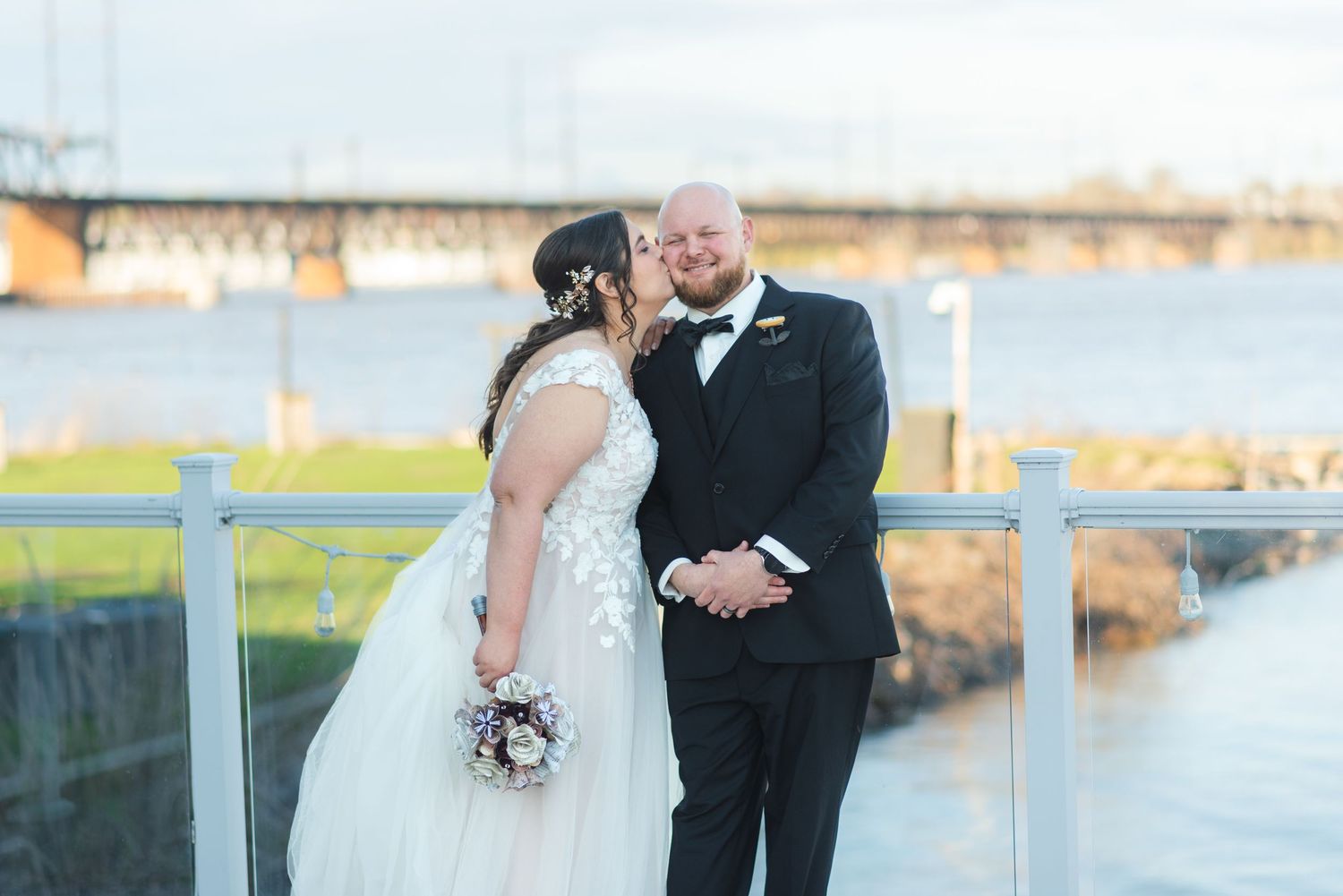 A newlywed couple. The bride is kissing the groom on his cheek.