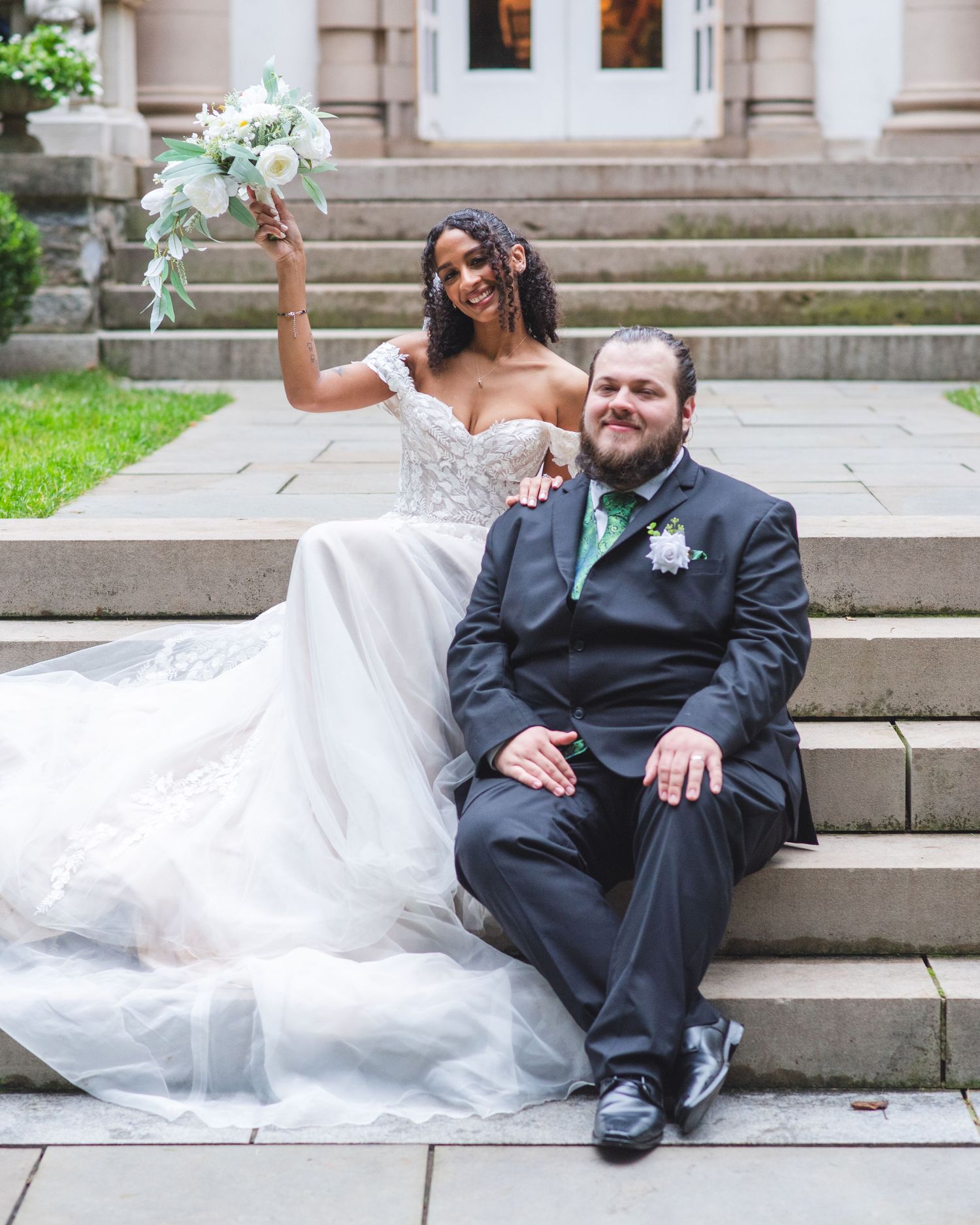A newlywed couple sitting together on some stairs.