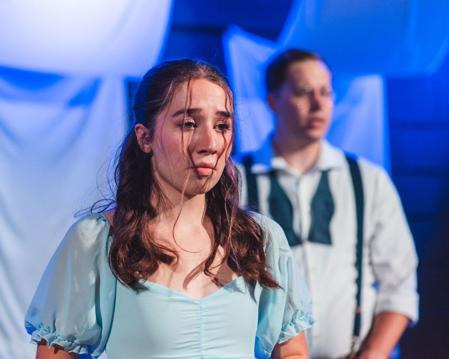 A photo from a production of Spring Awakening. The actress playing Wendla is in the foreground with the actor playing Melchior behind her.