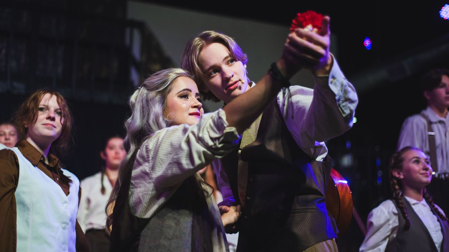 A photo from a production of Hadestown. The actors playing Orpheus and Eurydice are featured holding a carnation.
