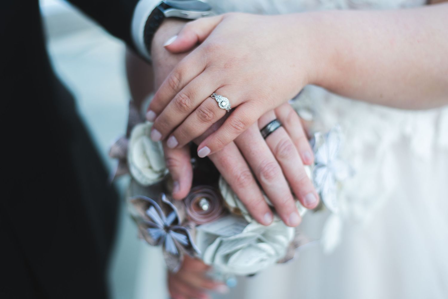 A newlywed couple crossing their hands over a bouquet made of pages of sheet music. They are showing off their new rings.