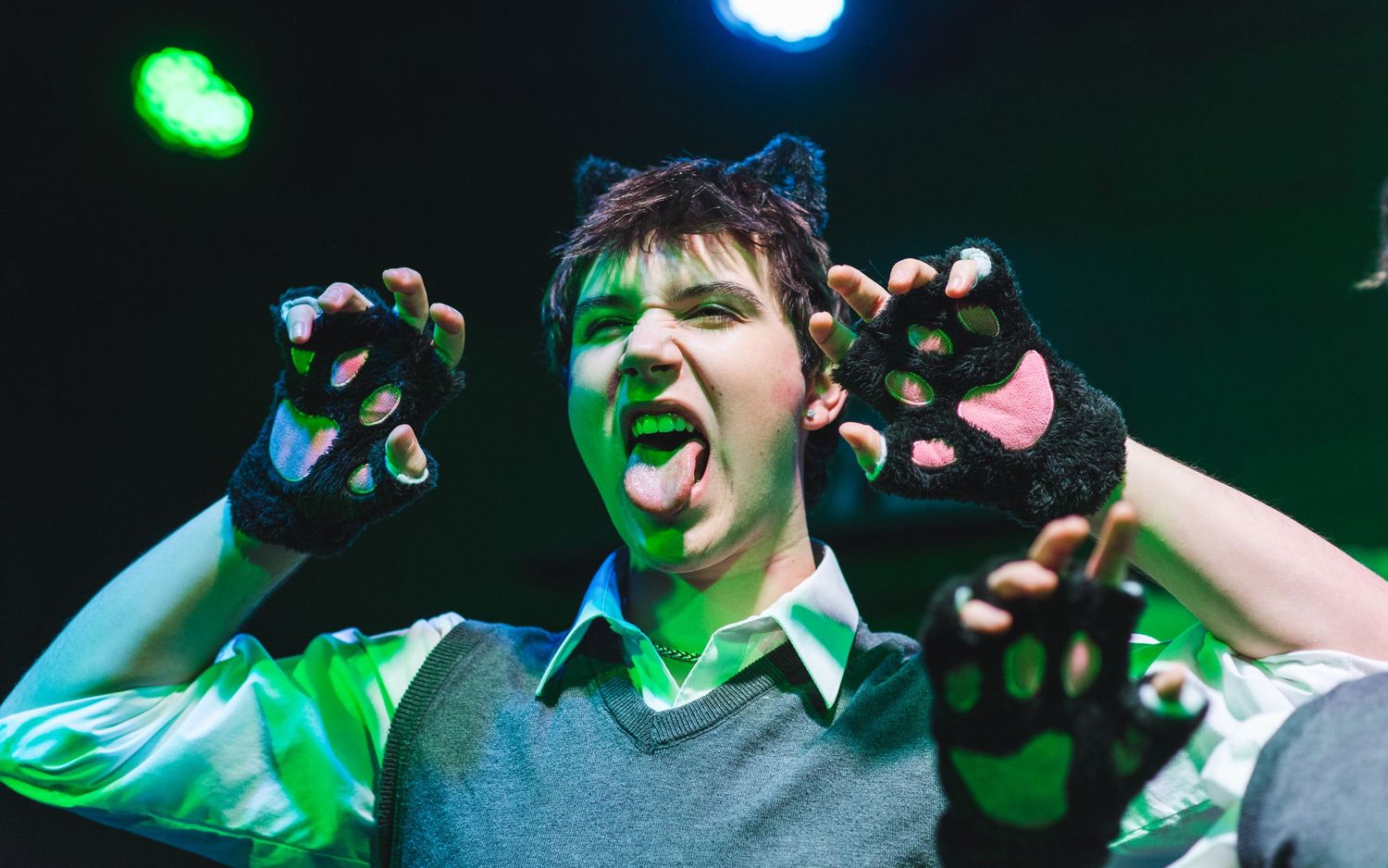 A photo from a production of Ride the Cyclone. An actor wearing cat ears and gloves is featured.