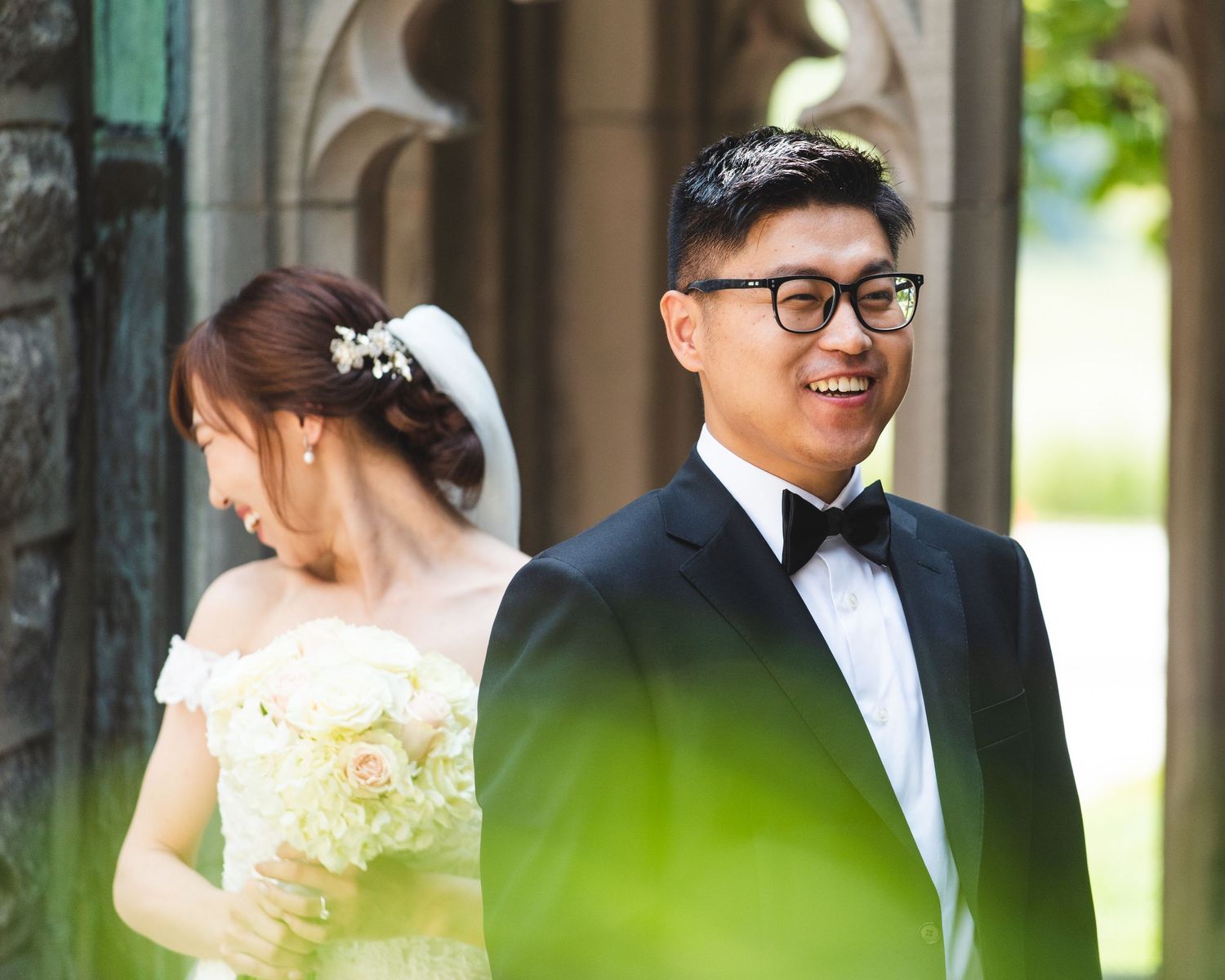 A bride and groom having a first look. The bride is laughing behind the groom.