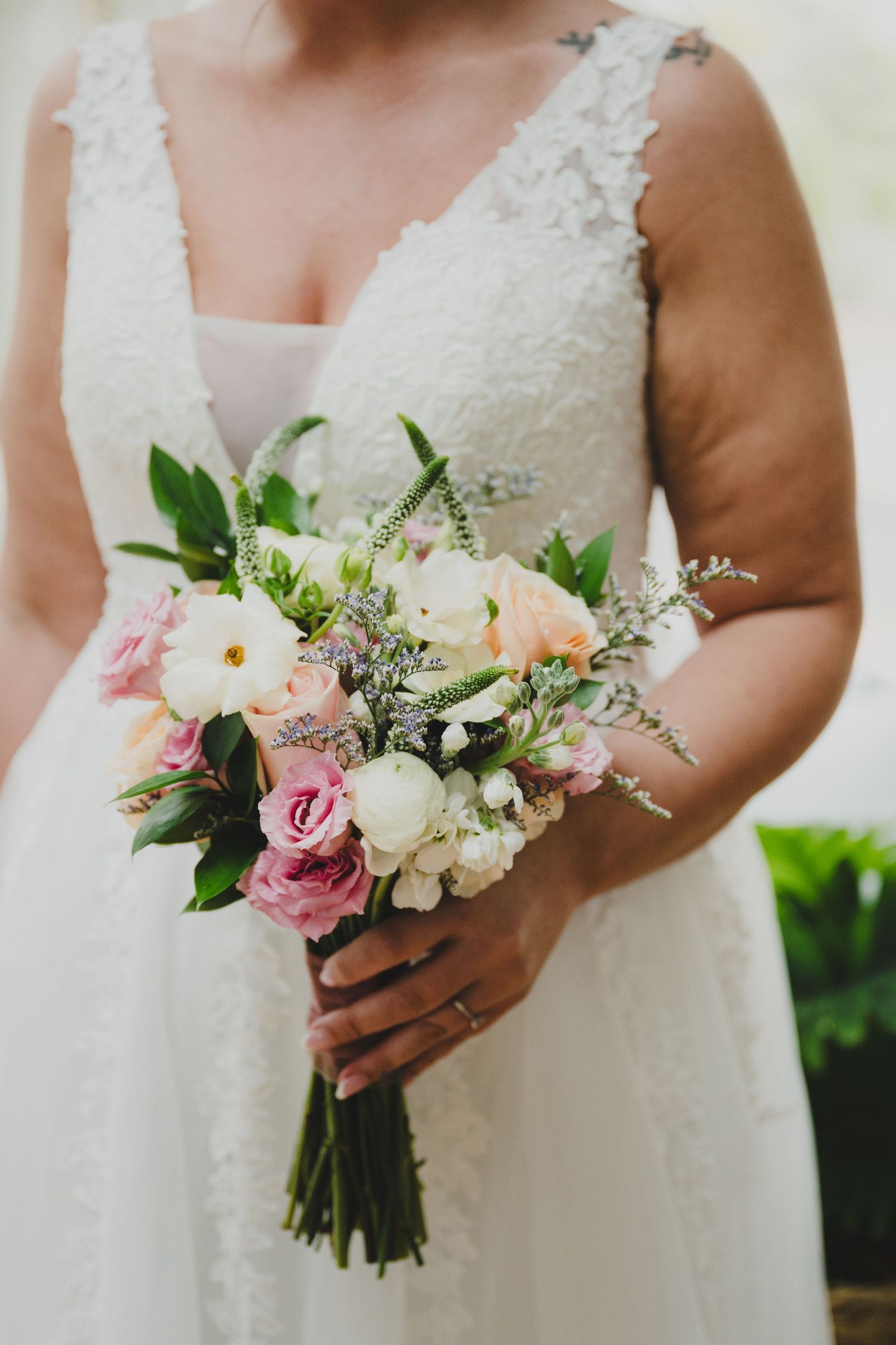 A row of wedding bouquets featuring pink and white roses with greenery held against white lace dresses.