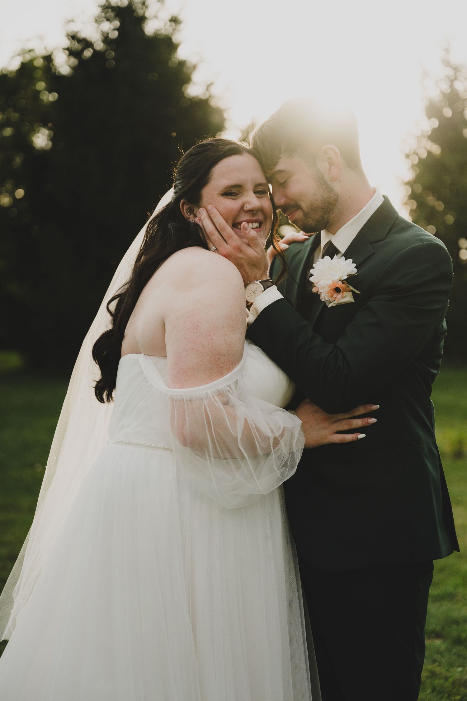 A romantic wedding couple embraces in a garden setting during golden hour as sunlight filters through trees.