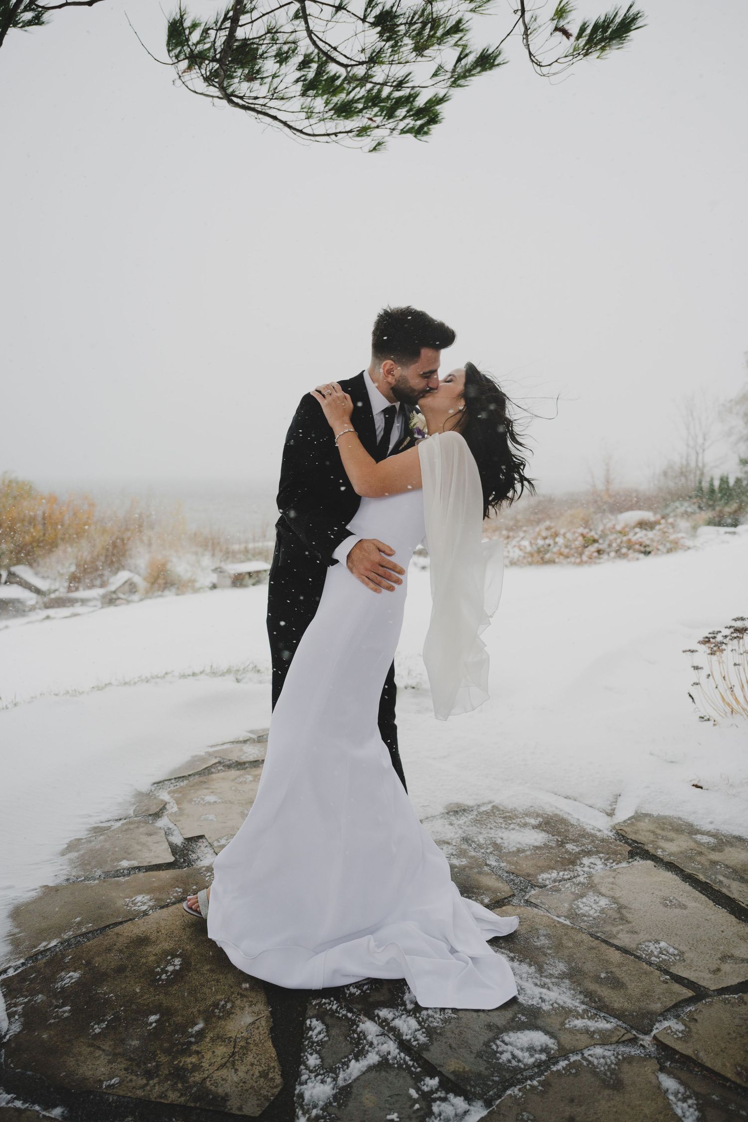 A couple in wedding attire embrace on snowy rocks during their winter mountain elopement photoshoot.