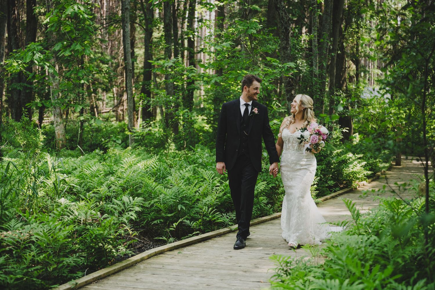 A couple walks down a winding garden path surrounded by lush green foliage in a romantic outdoor setting.