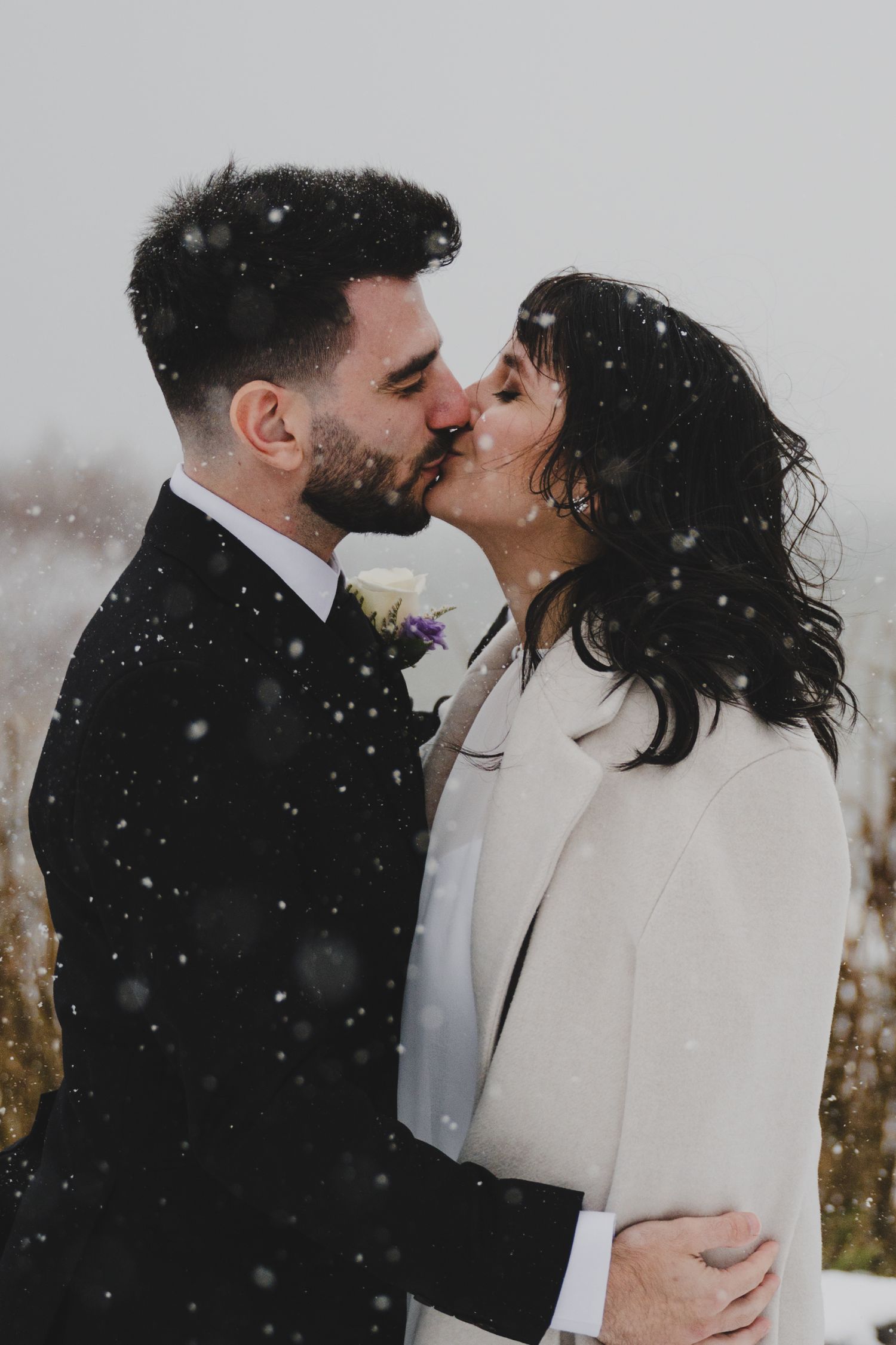 A romantic winter wedding couple sharing tender kisses in the snow with a dreamy, ethereal atmosphere.