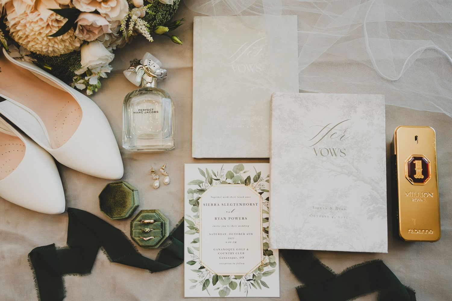 Wedding details flatlay with white invitation, perfume bottle, shoes and floral accents on light surface.